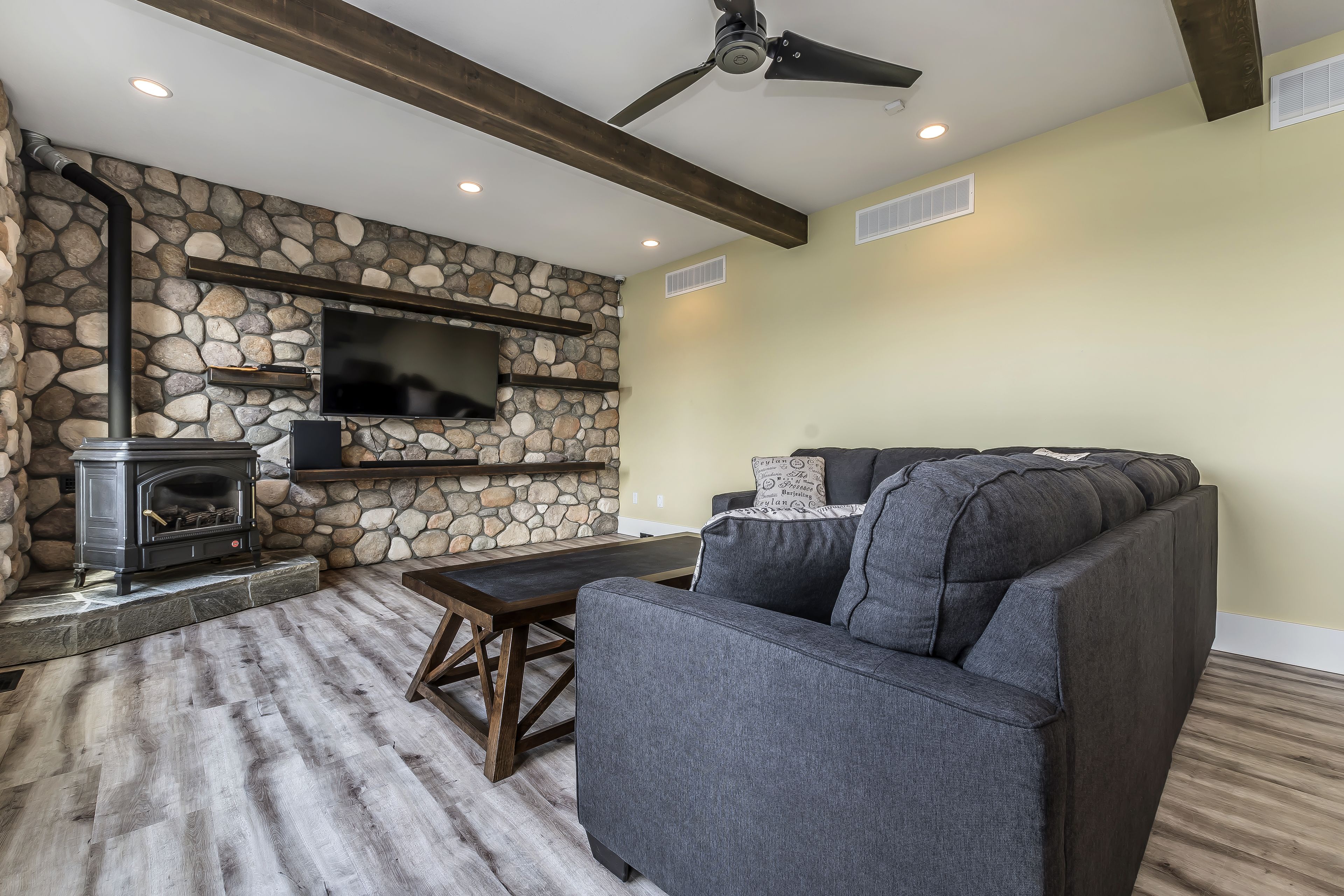 Un salon avec un mur en pierre, une cheminée, un canapé et un ventilateur de plafond.