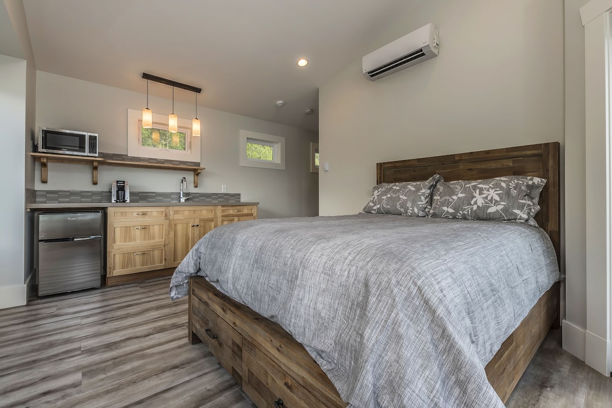 Ein Schlafzimmer mit einem Holzbett, einer grauen Bettdecke und einem Nachttisch aus Holz.