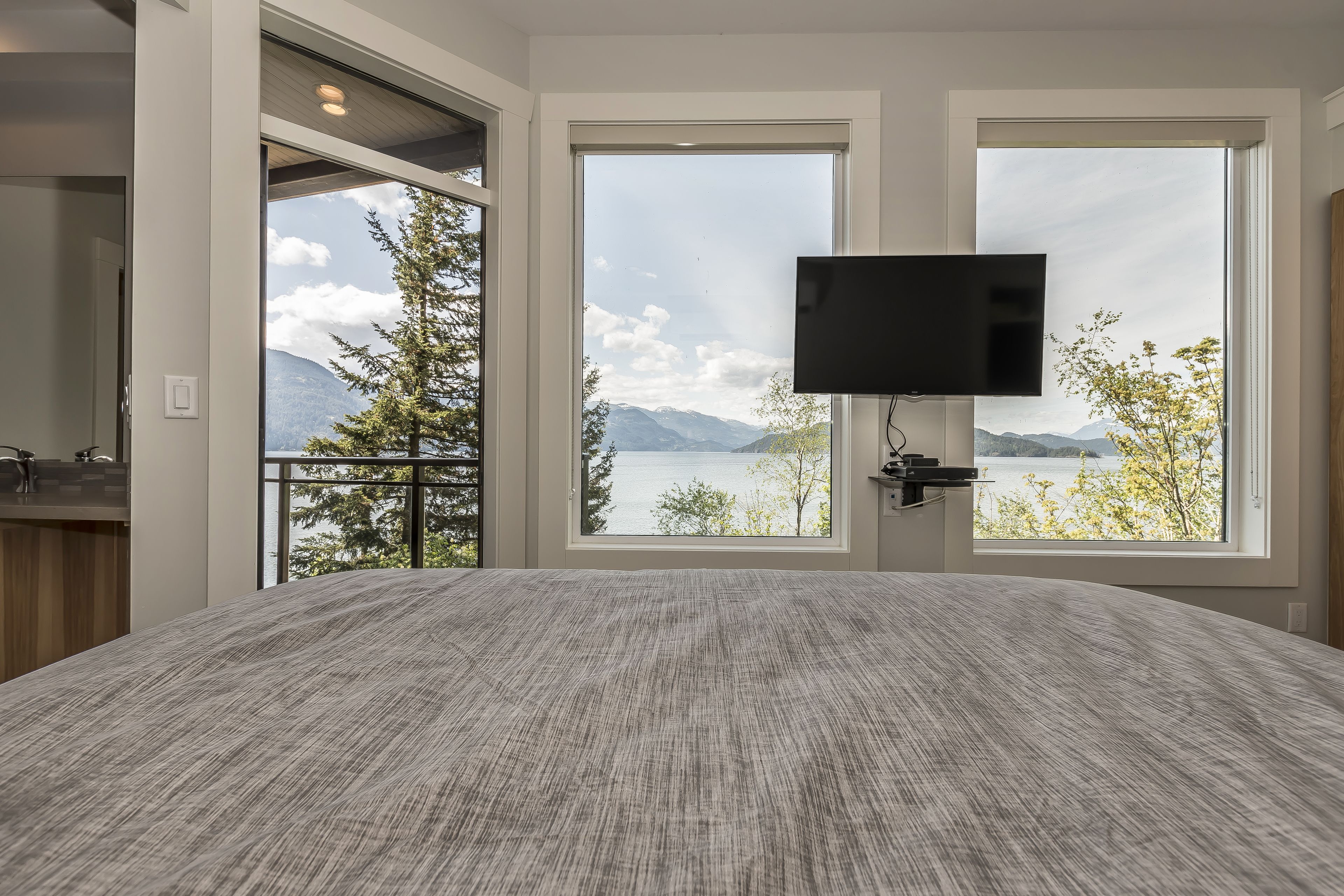 A bedroom with a large bed, a TV mounted on the wall, and a window with a mountain view.