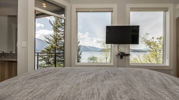 A bedroom with a large bed, a TV mounted on the wall, and a window with a mountain view.