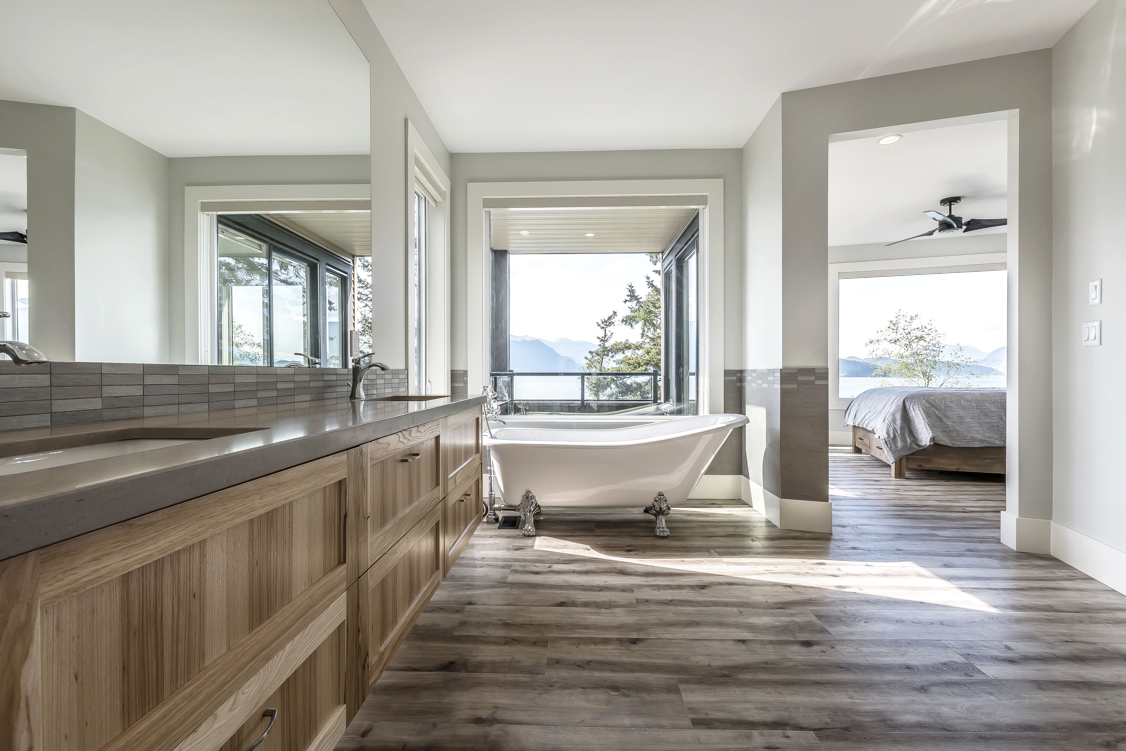 A modern bathroom with a freestanding bathtub, wooden cabinetry, and large windows offering a mountain view.