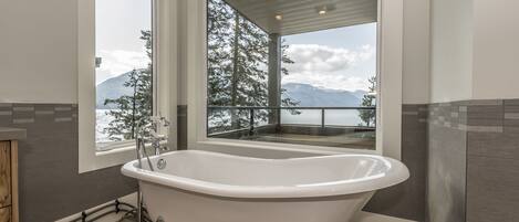 A modern bathroom with a freestanding bathtub, large windows, and a view of mountains.