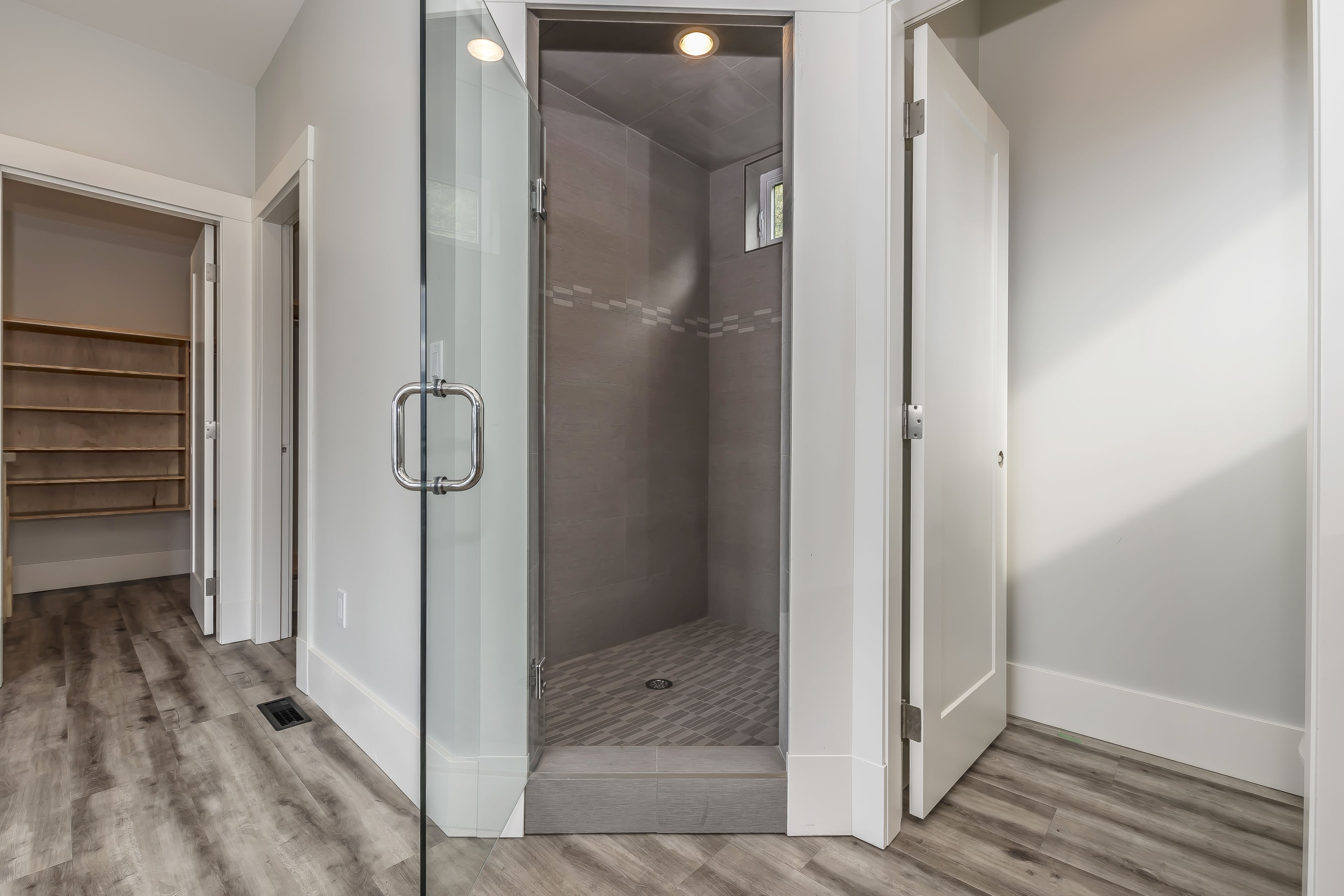 A walk-in closet with wooden shelves and a glass door leading to a shower area with a tiled floor.