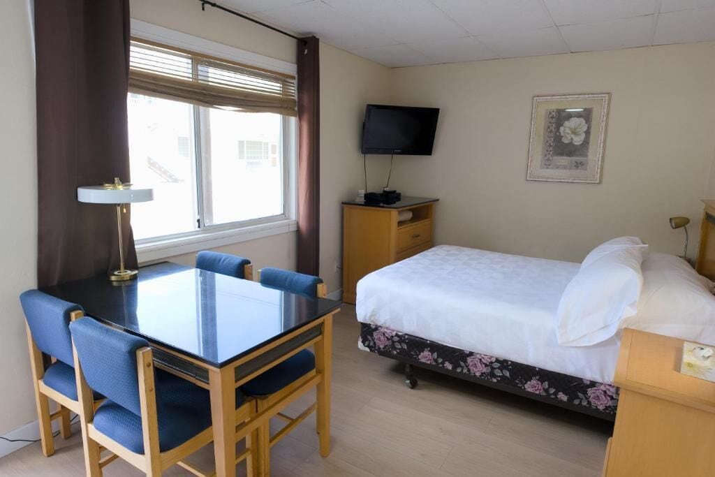 Una habitación de hotel con cama, televisor, escritorio con sillas y ventana con cortinas.