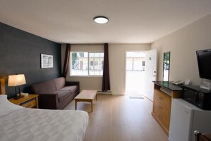 A hotel room with a bed, a sofa, a desk, a television, and a kitchenette. - Park Motel (Hope)