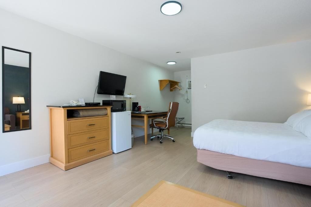 Ein Hotelzimmer mit einem Bett, einem Schreibtisch mit Computer, einem Fernseher und einem kleinen Kühlschrank.