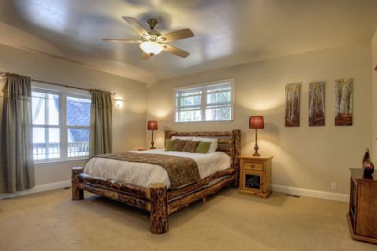 A bedroom with a large bed, a ceiling fan, two bedside tables with lamps, and a window with curtains.
