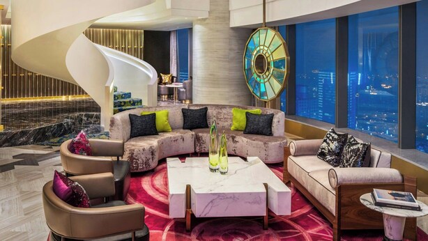 Een moderne hotel lobby met een centrale zithoek, een wenteltrap en grote ramen met uitzicht op de stad.