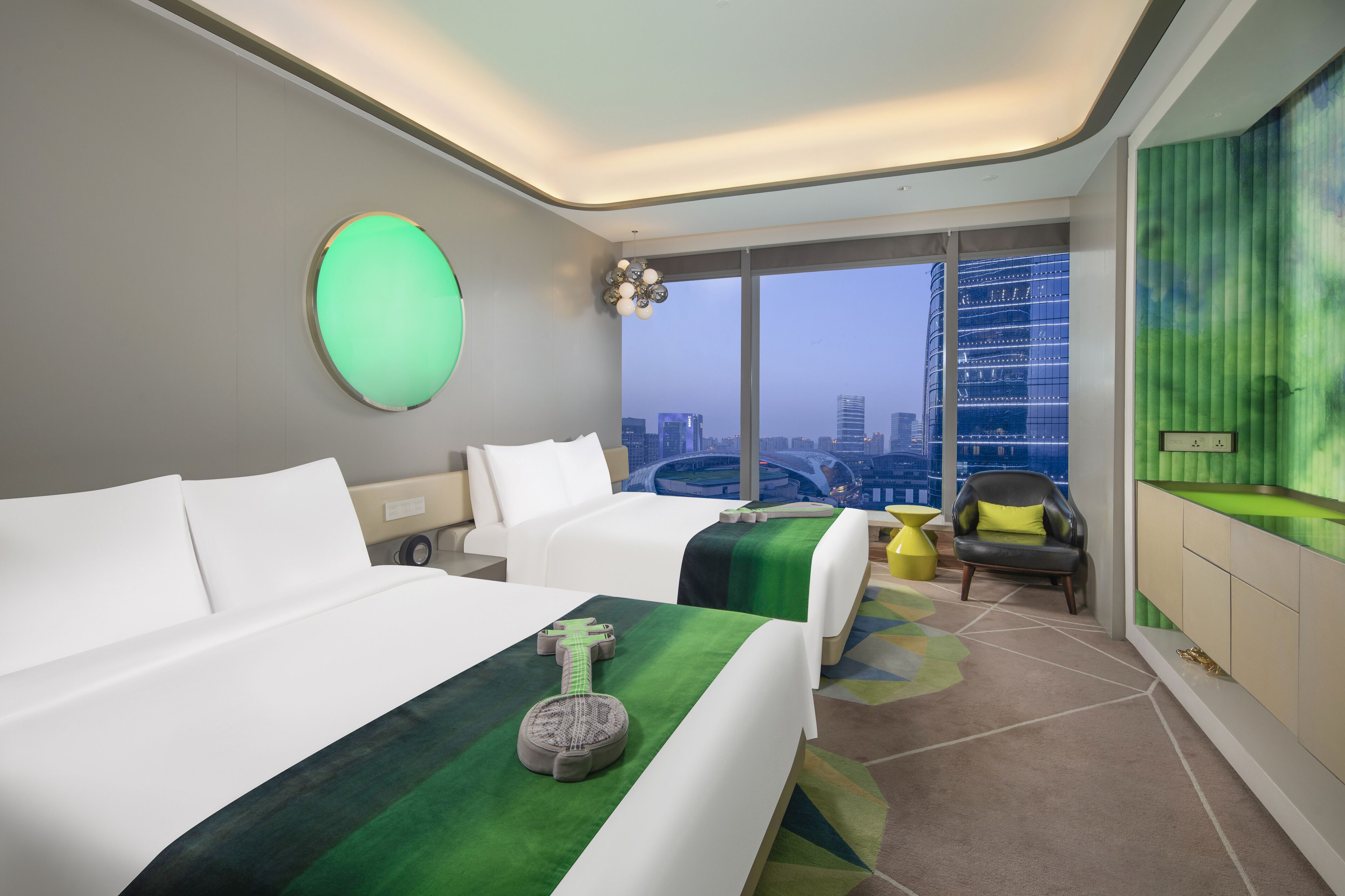 A modern hotel room with two beds, a city view, and a green accent wall.
