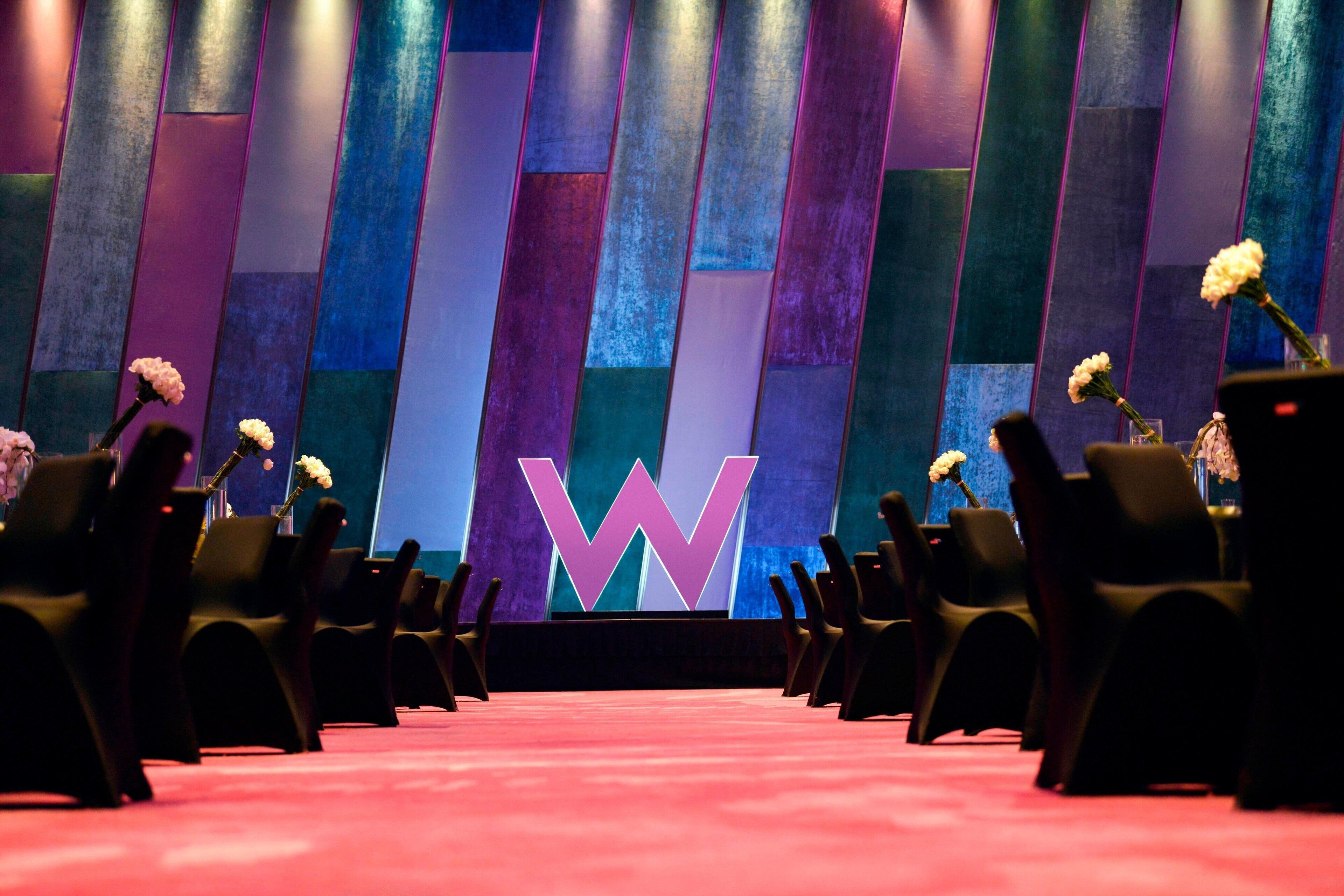 Un salón de conferencias con filas de sillas y un gran logotipo de 'W' en el fondo.