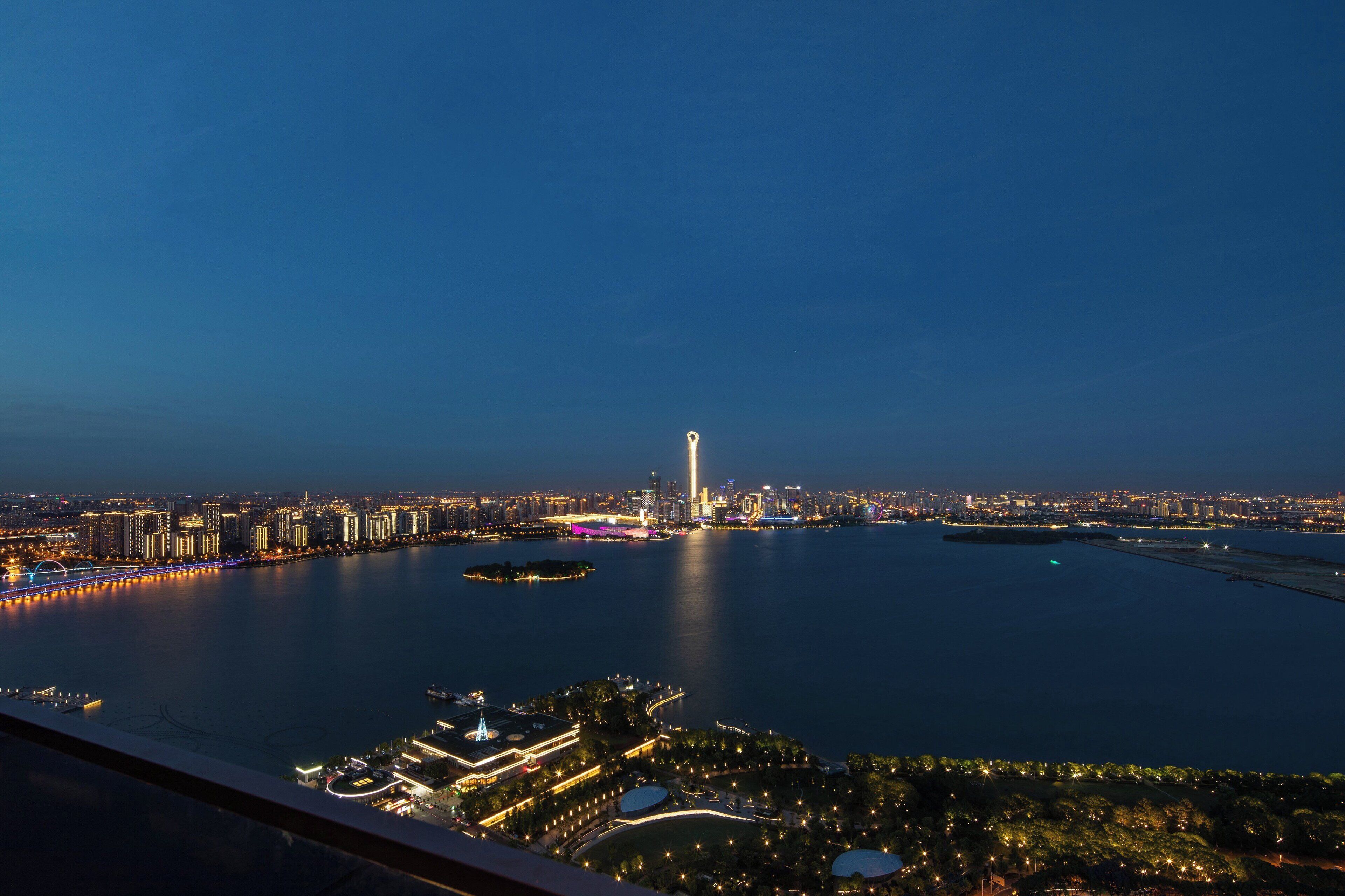 A nighttime cityscape with a prominent tower, a bridge, and a body of water.