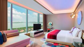 Ein modernes Hotelzimmer mit einem großen Bett, einem Fernseher, einer Couch und Blick auf die Stadt.