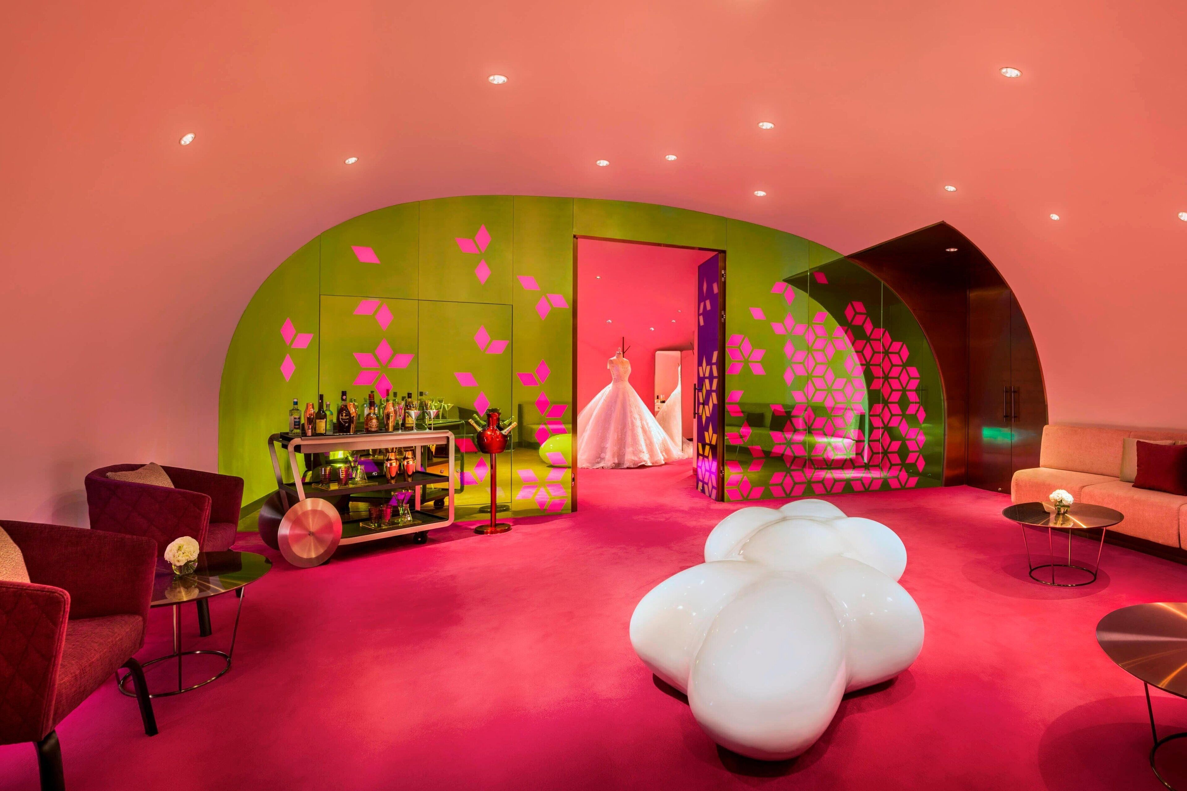 A modern interior with a vibrant pink and green color scheme, featuring a bar area, seating, and a unique white spherical chair.