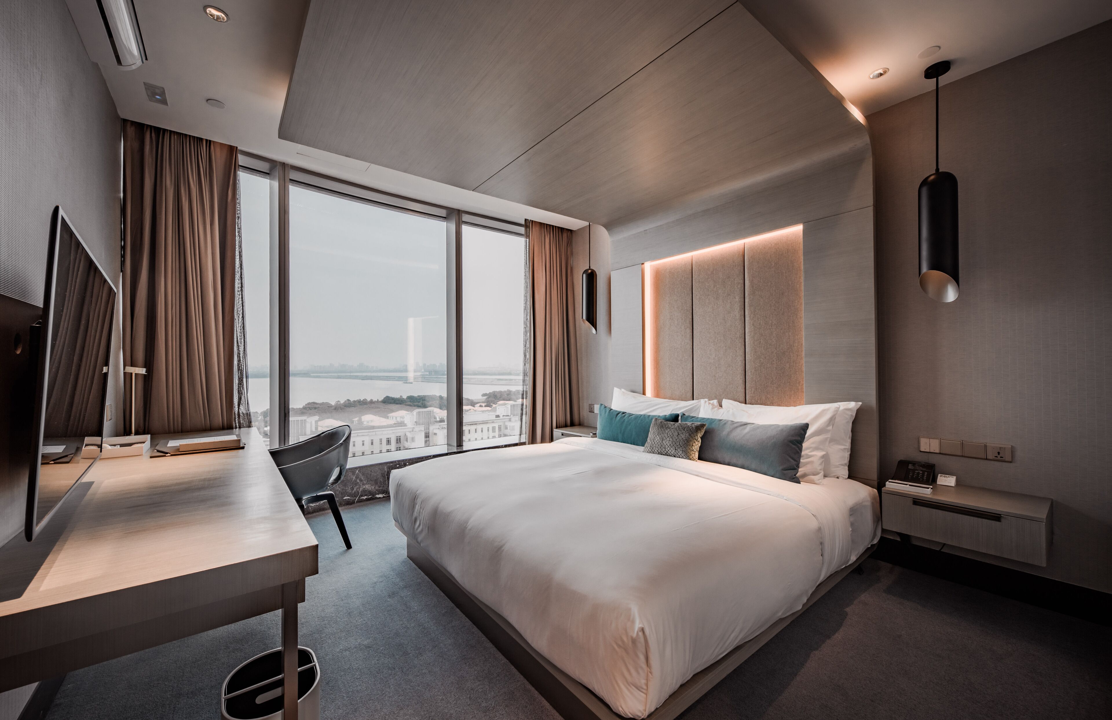A modern hotel room with a large bed, a desk, and a view of a cityscape.