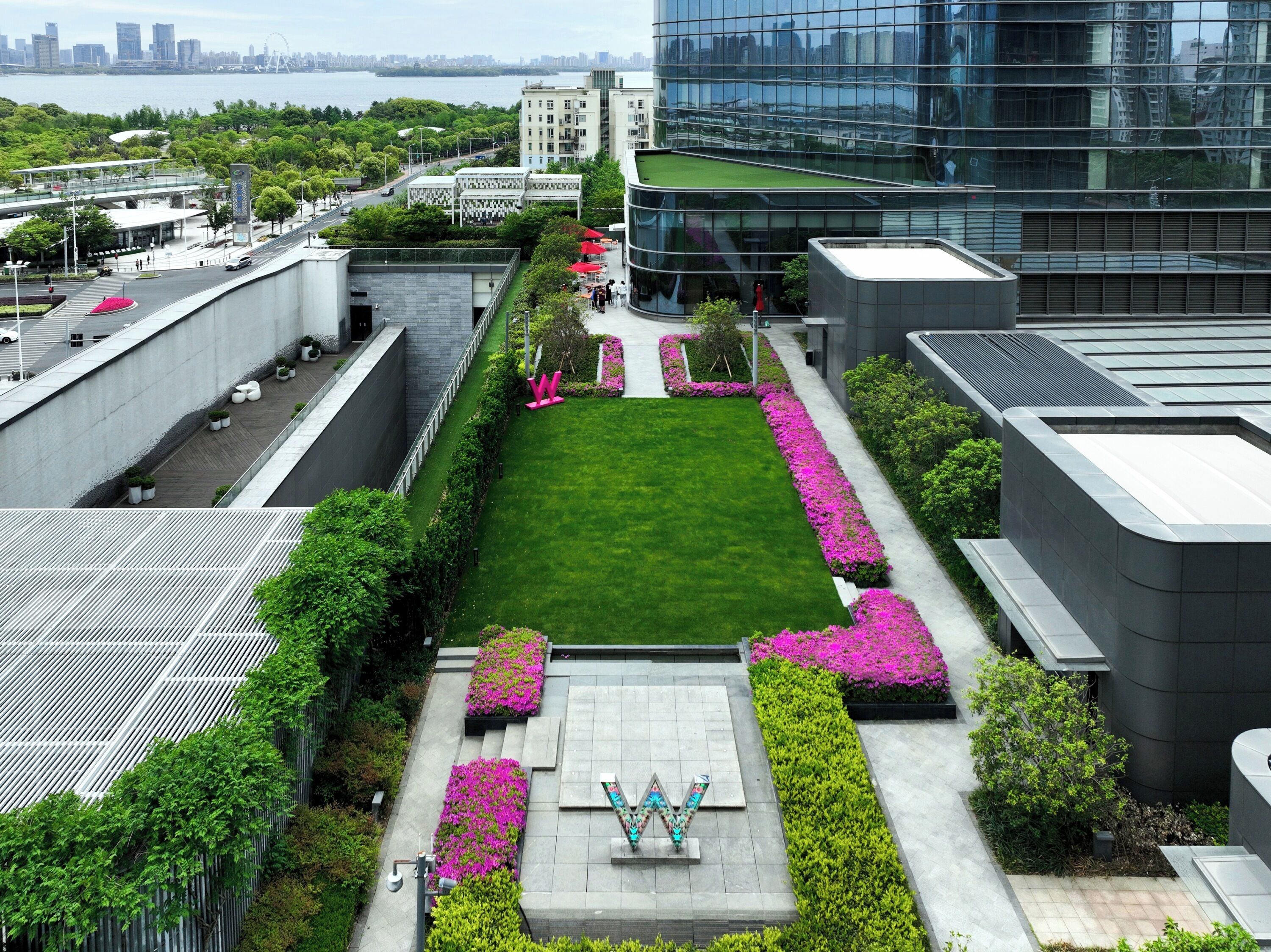 Un bâtiment moderne doté d’un jardin sur le toit, d’une pelouse centrale et d’un sentier bordé de fleurs roses.
