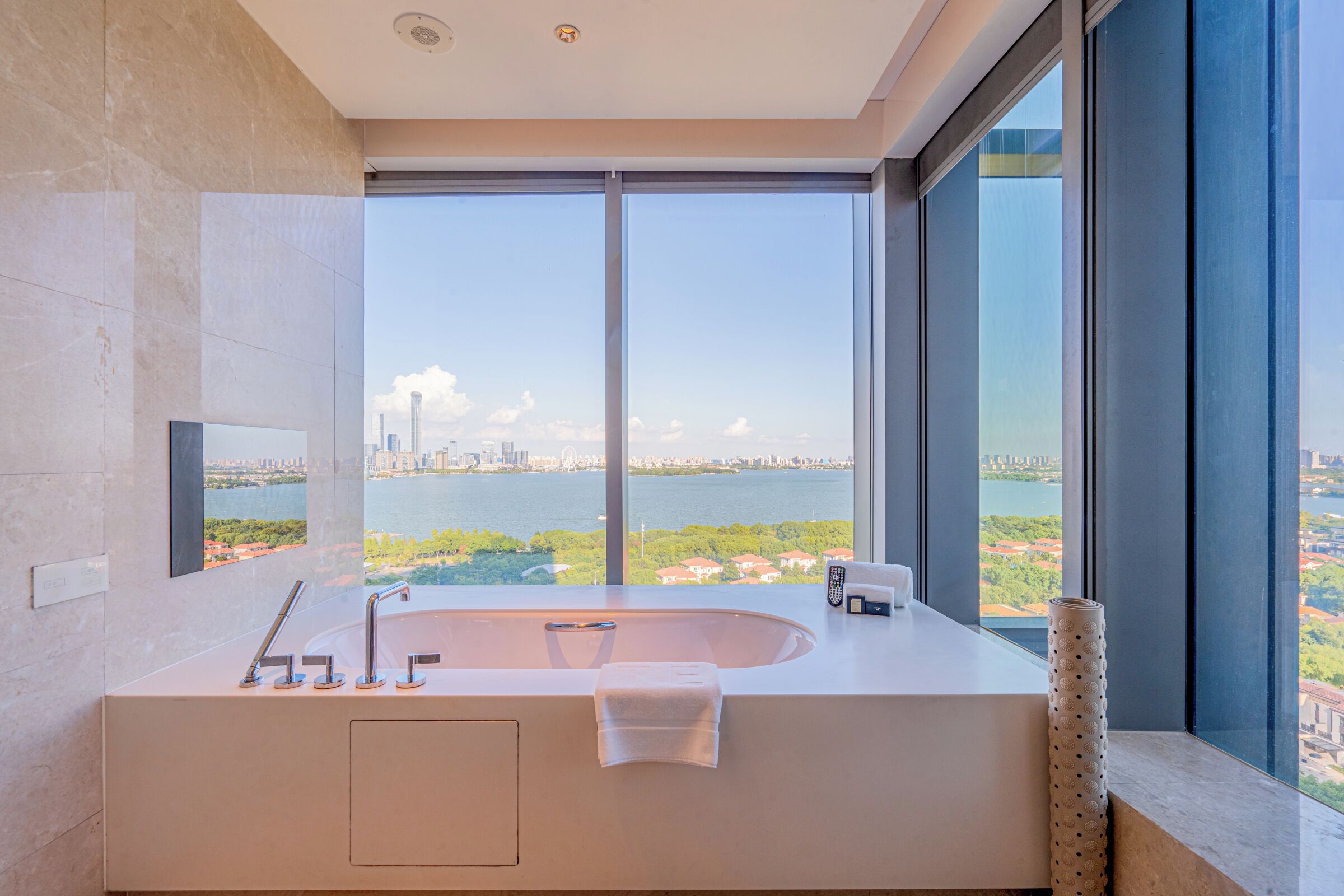 Un baño moderno con una bañera grande, un espejo y vistas a un paisaje urbano y una masa de agua.