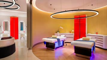 A modern spa room with two treatment beds, a reception area, and a mirror.