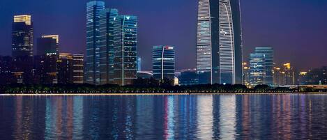 A nighttime cityscape with modern skyscrapers reflected in a body of water.