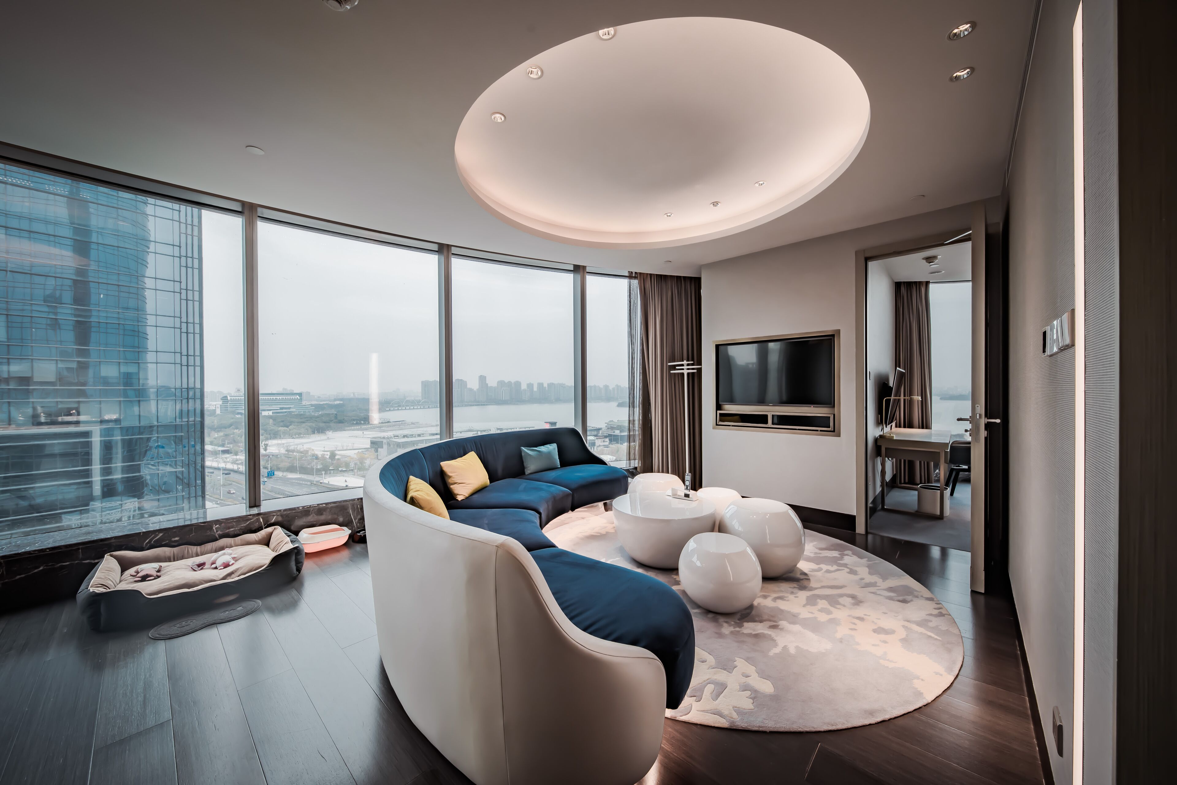 A modern living room with a curved sofa, a round coffee table, and a large window offering a city view.