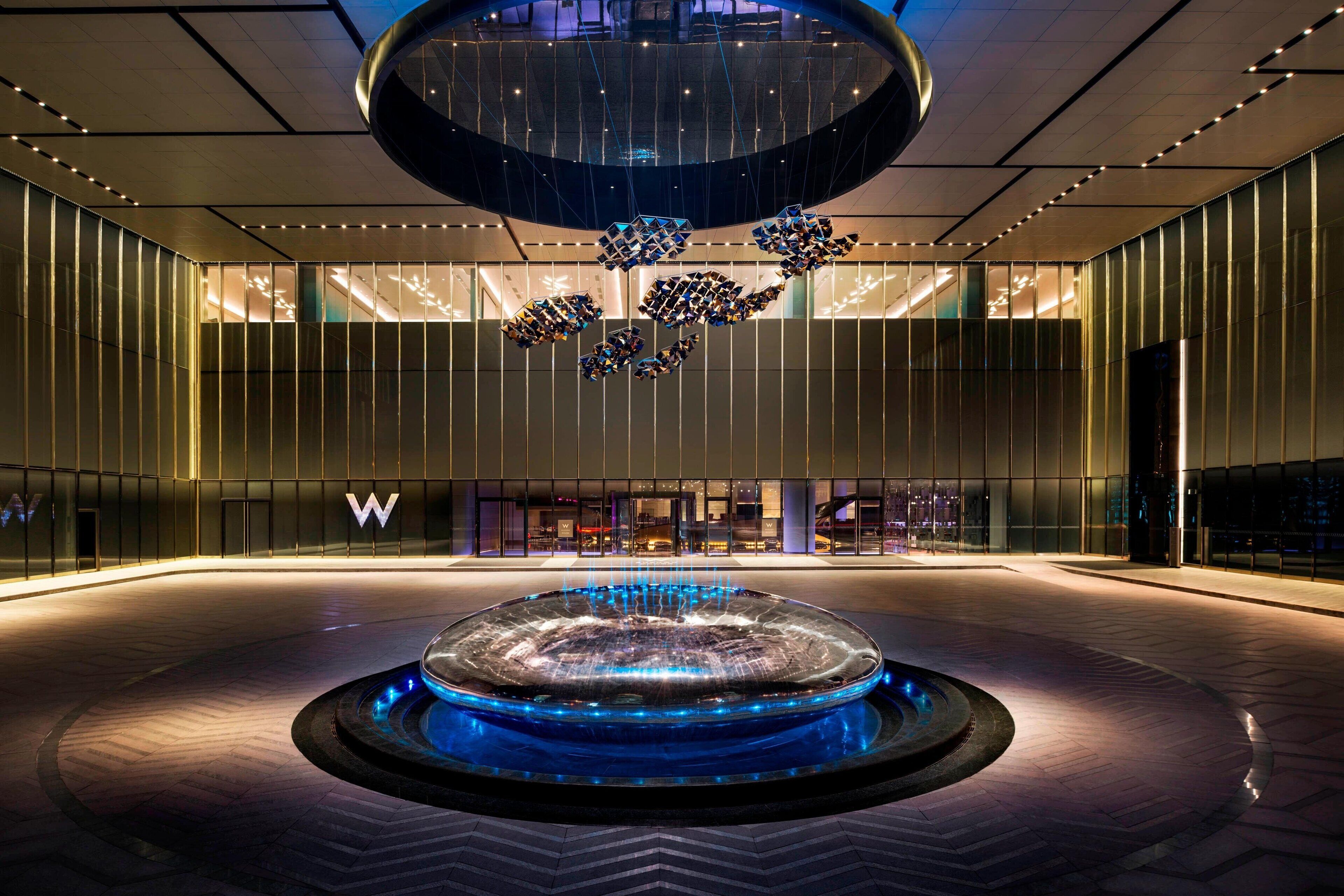 Un moderno vestíbulo de hotel con una fuente central, un diseño de techo circular grande y un llamativo logotipo 'W' en la pared.