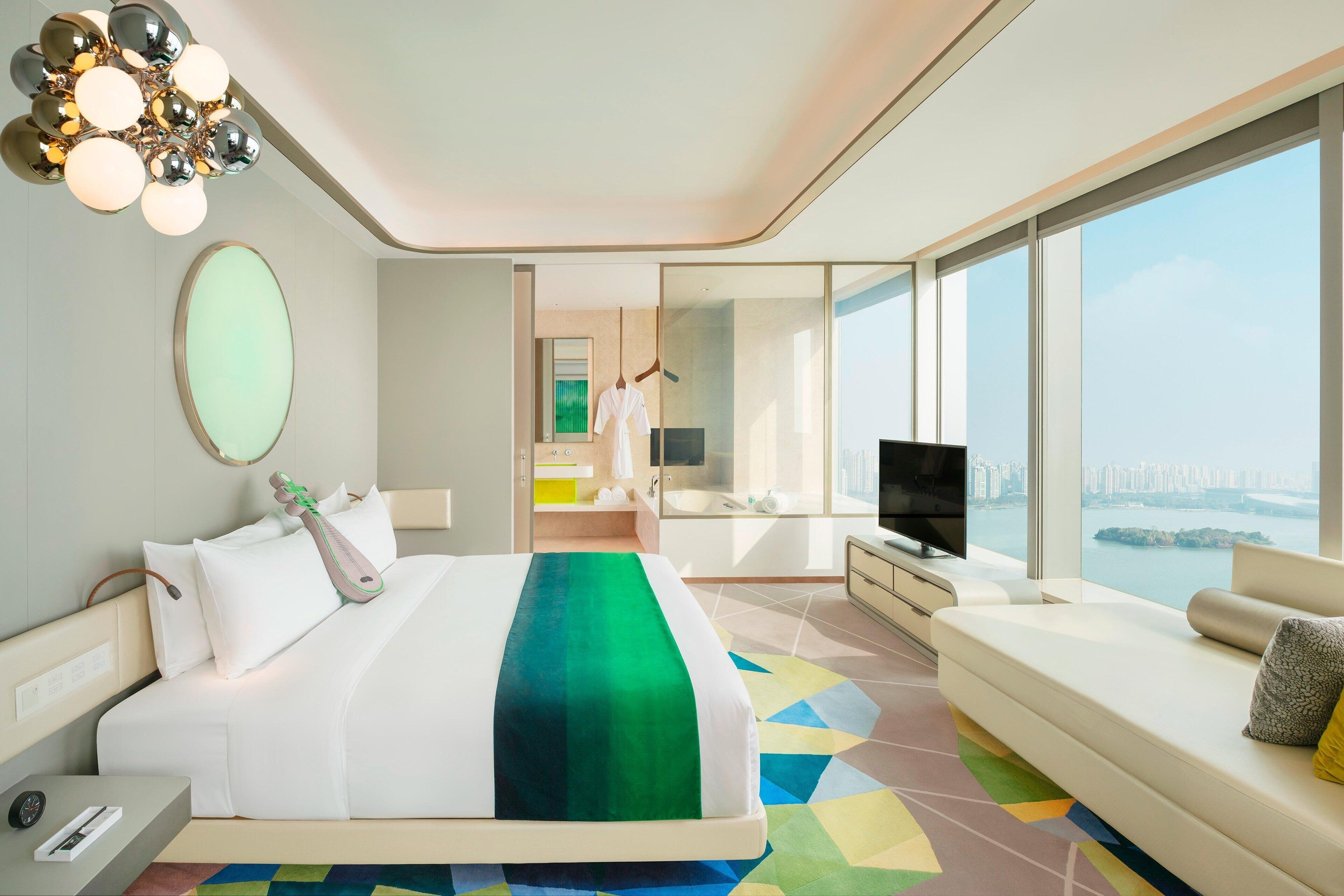 Een moderne hotelkamer met een groot bed, een bank, een televisie en uitzicht op de stad.