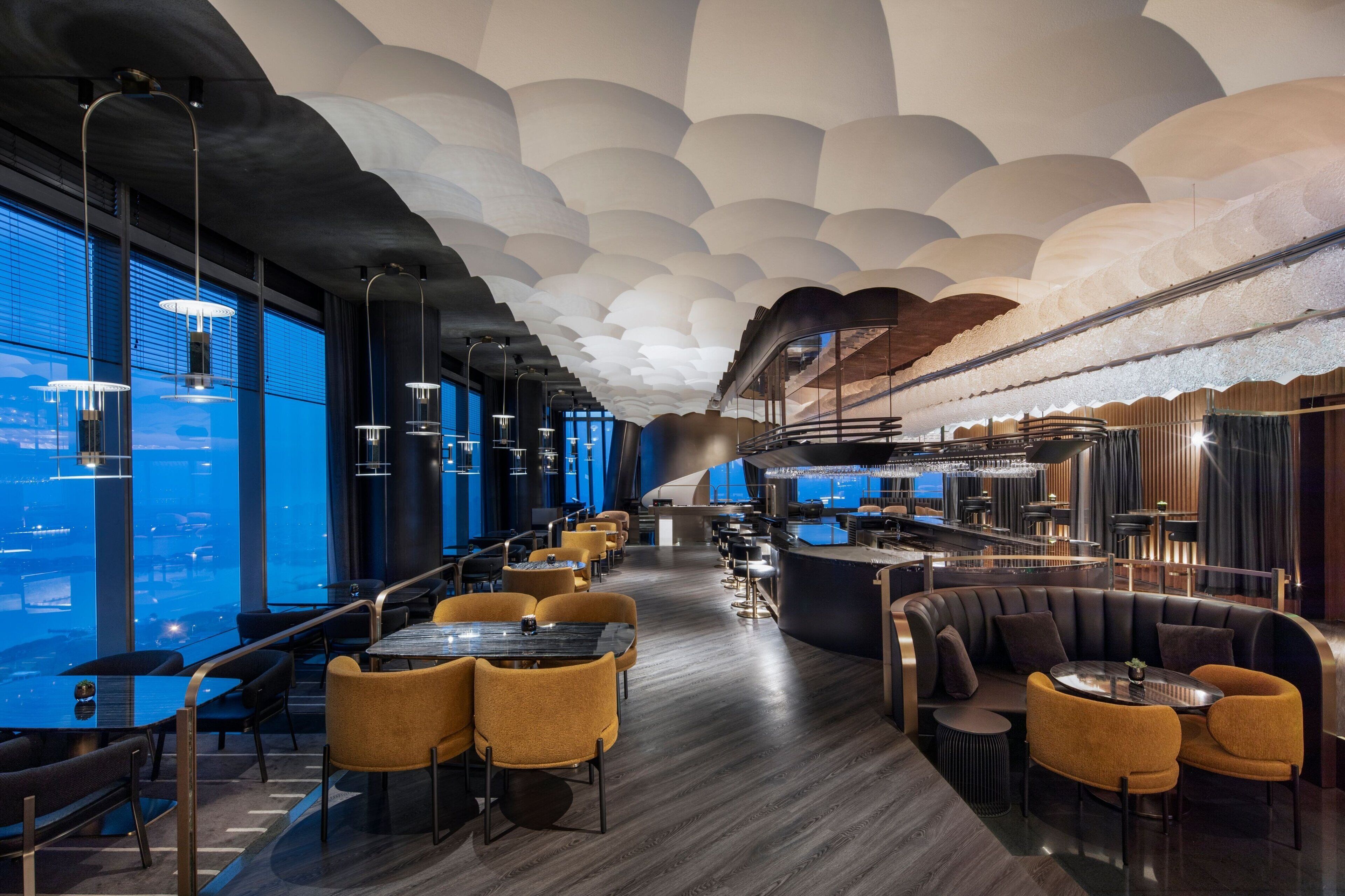 A modern restaurant with a unique ceiling design, large windows, and a bar area.