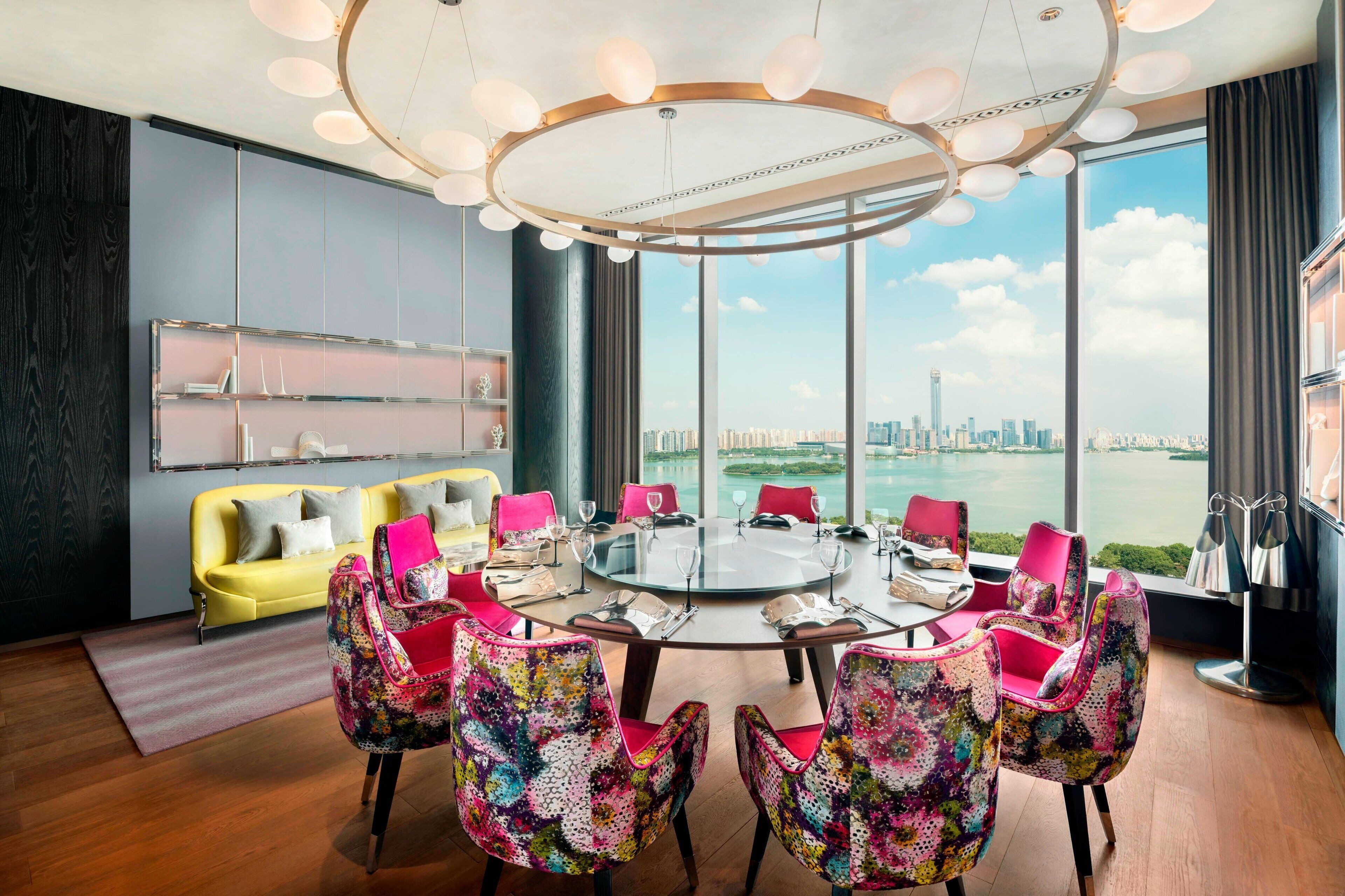Une salle de réunion moderne avec une table en verre, des chaises colorées, un canapé jaune et une vue sur la ville.