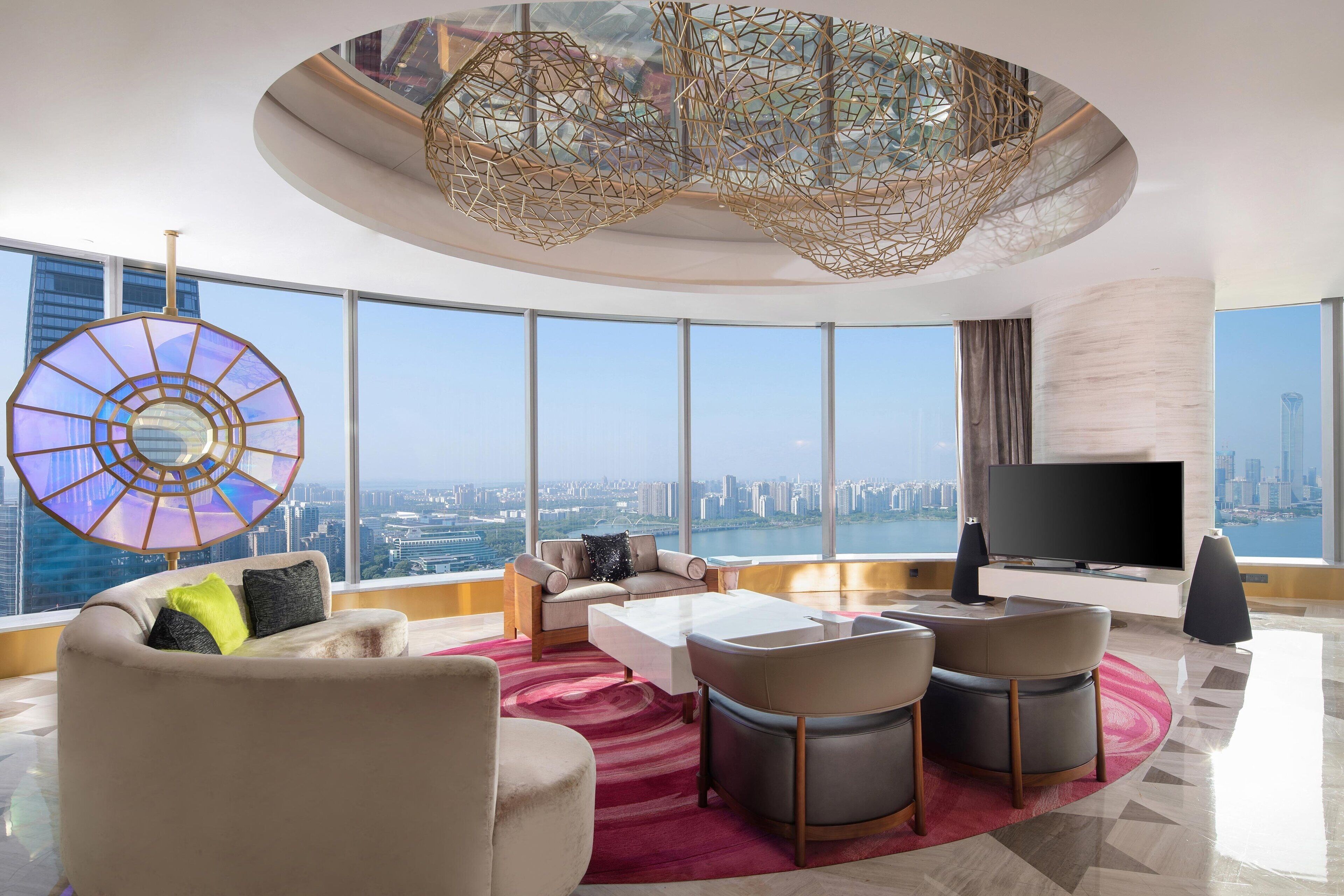 A modern living room with a city view, a large TV, and a unique ceiling light fixture.