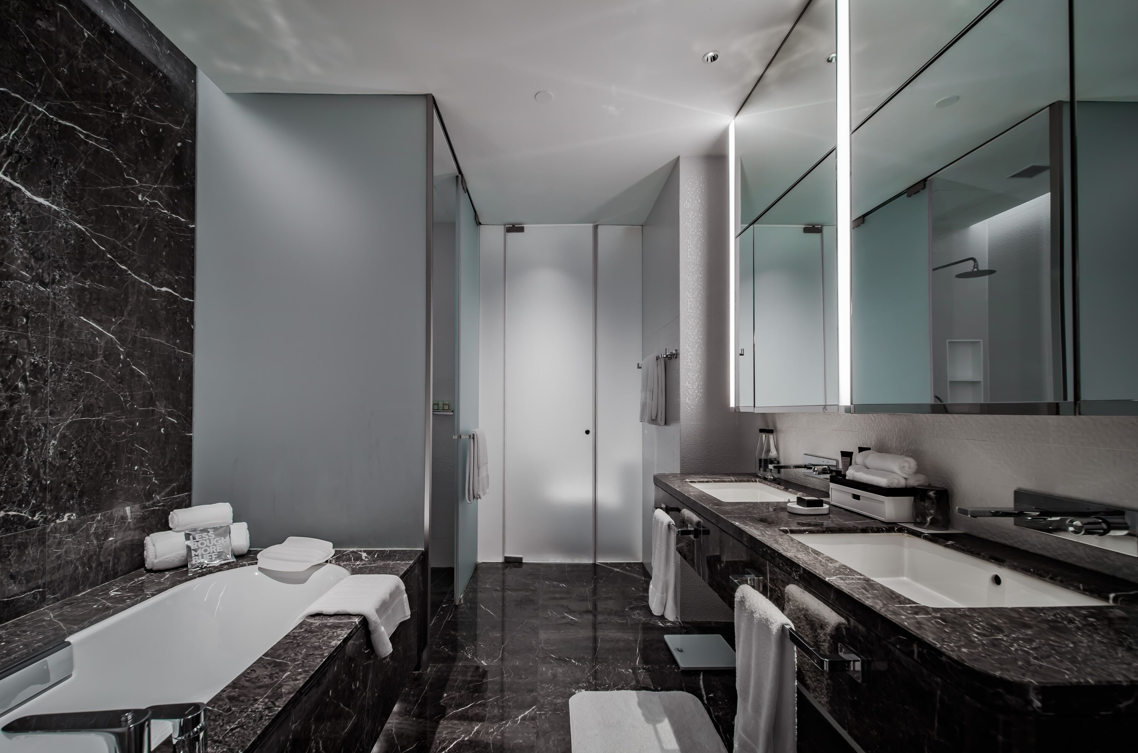 A modern bathroom with a large mirror, two sinks, a bathtub, and marble flooring.