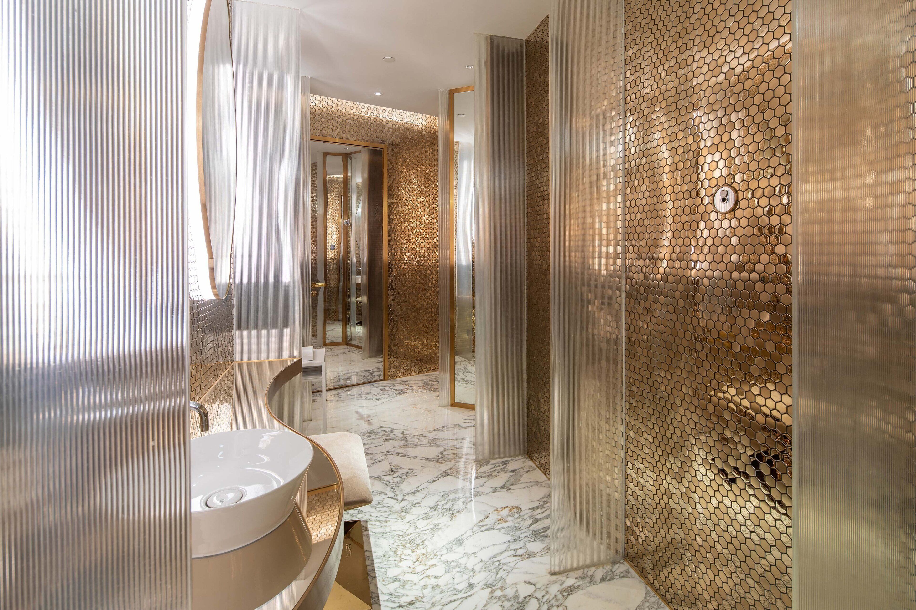 Un baño moderno con un espejo grande, un lavabo blanco y un suelo de mármol.