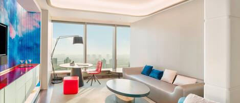 A modern living room with a sofa, a round coffee table, a red ottoman, a TV, and a city view through large windows.