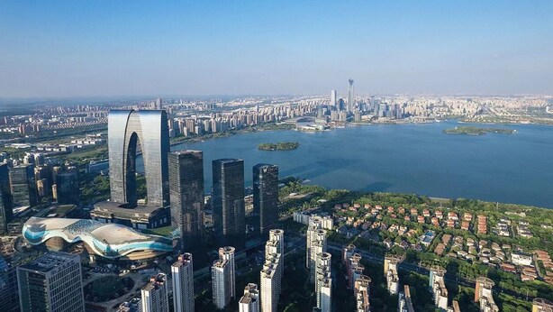 A cityscape with modern high-rise buildings, a distinctive curved structure, and a body of water. - W Suzhou (Suzhou)