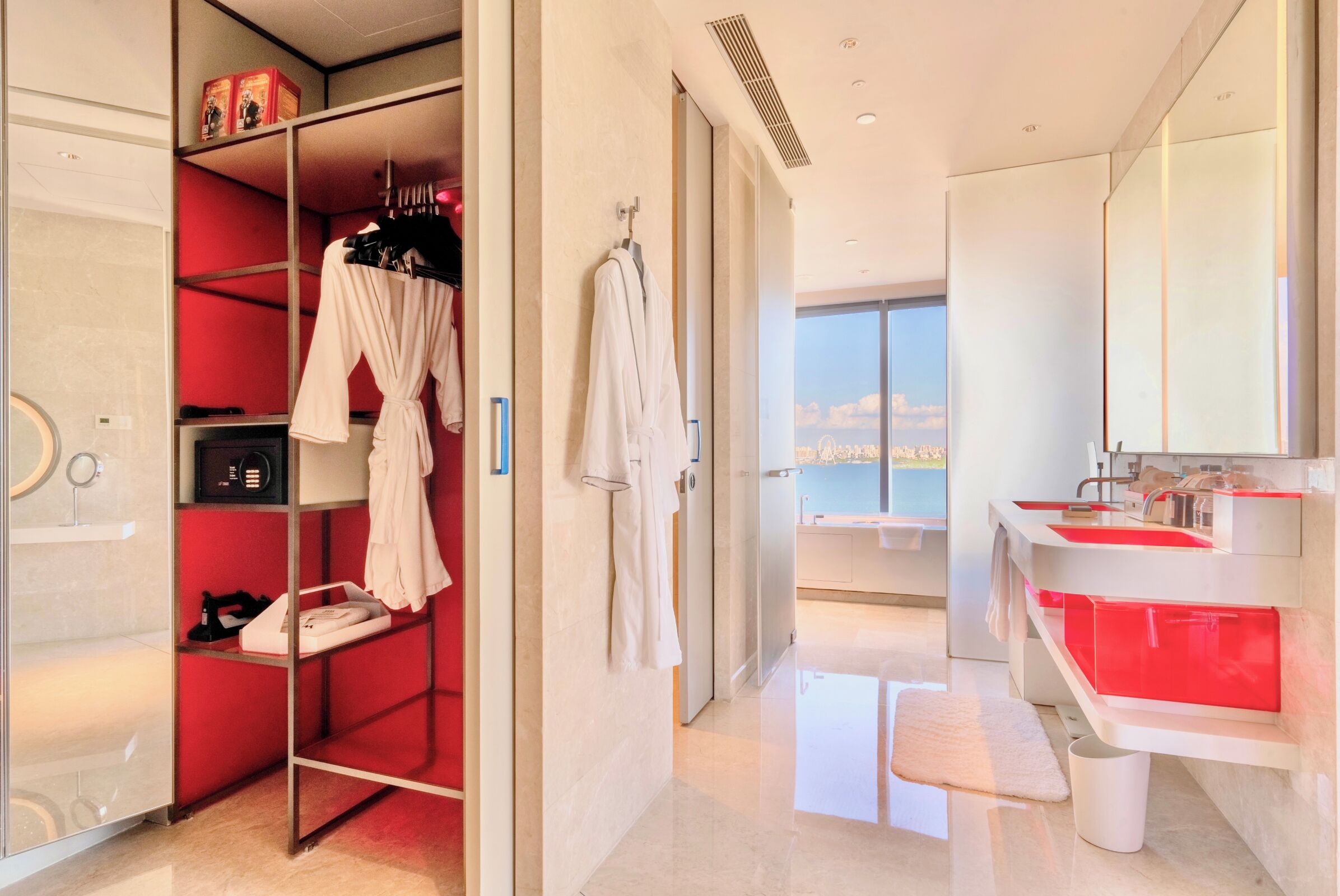 A modern bathroom with a large mirror, red accents, and a view of the city.
