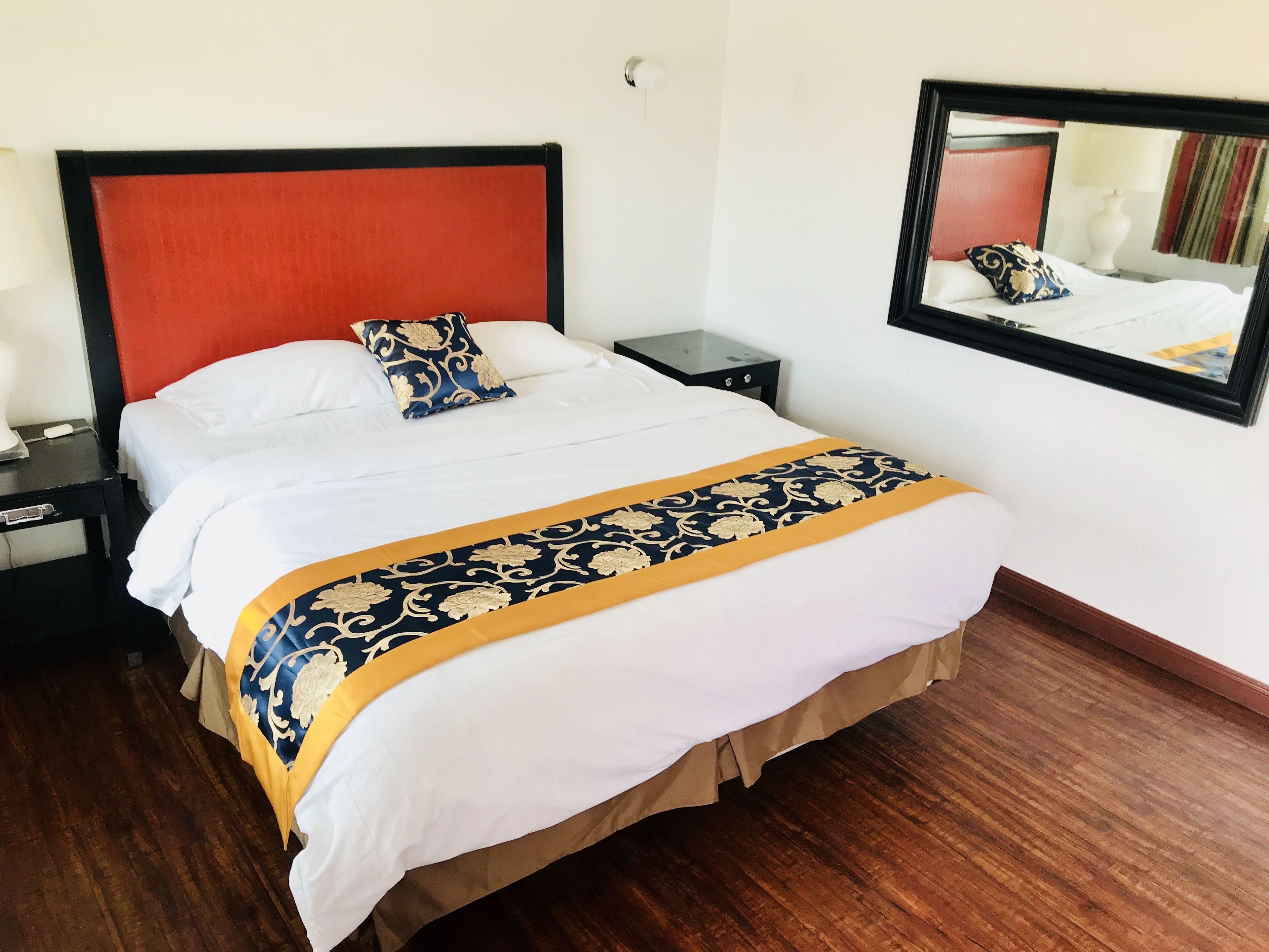 A hotel room with a large bed, a nightstand, a lamp, and a mirror on the wall.
