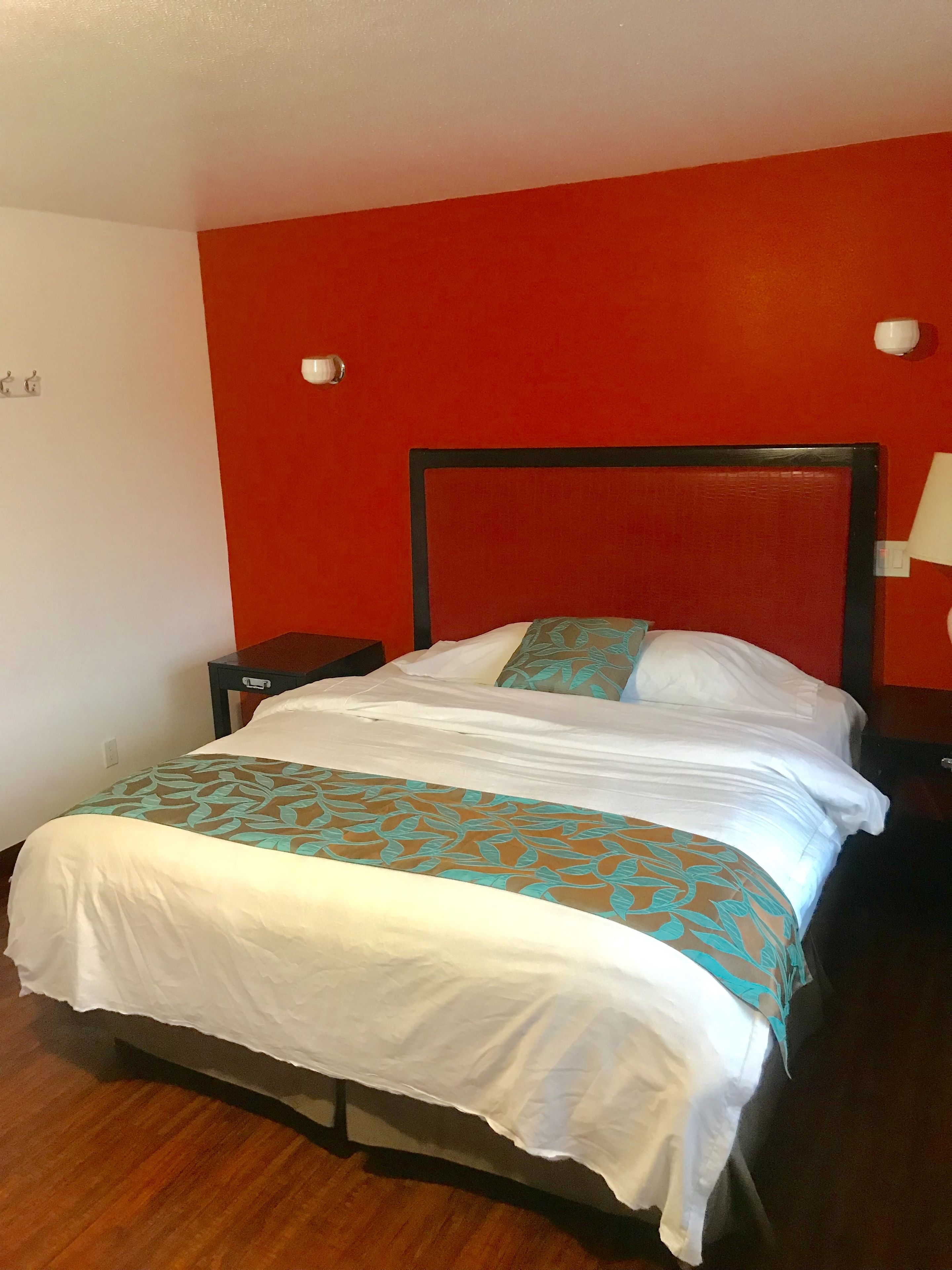 A single bed with a white and teal patterned bedspread in a room with red walls and a wooden floor.