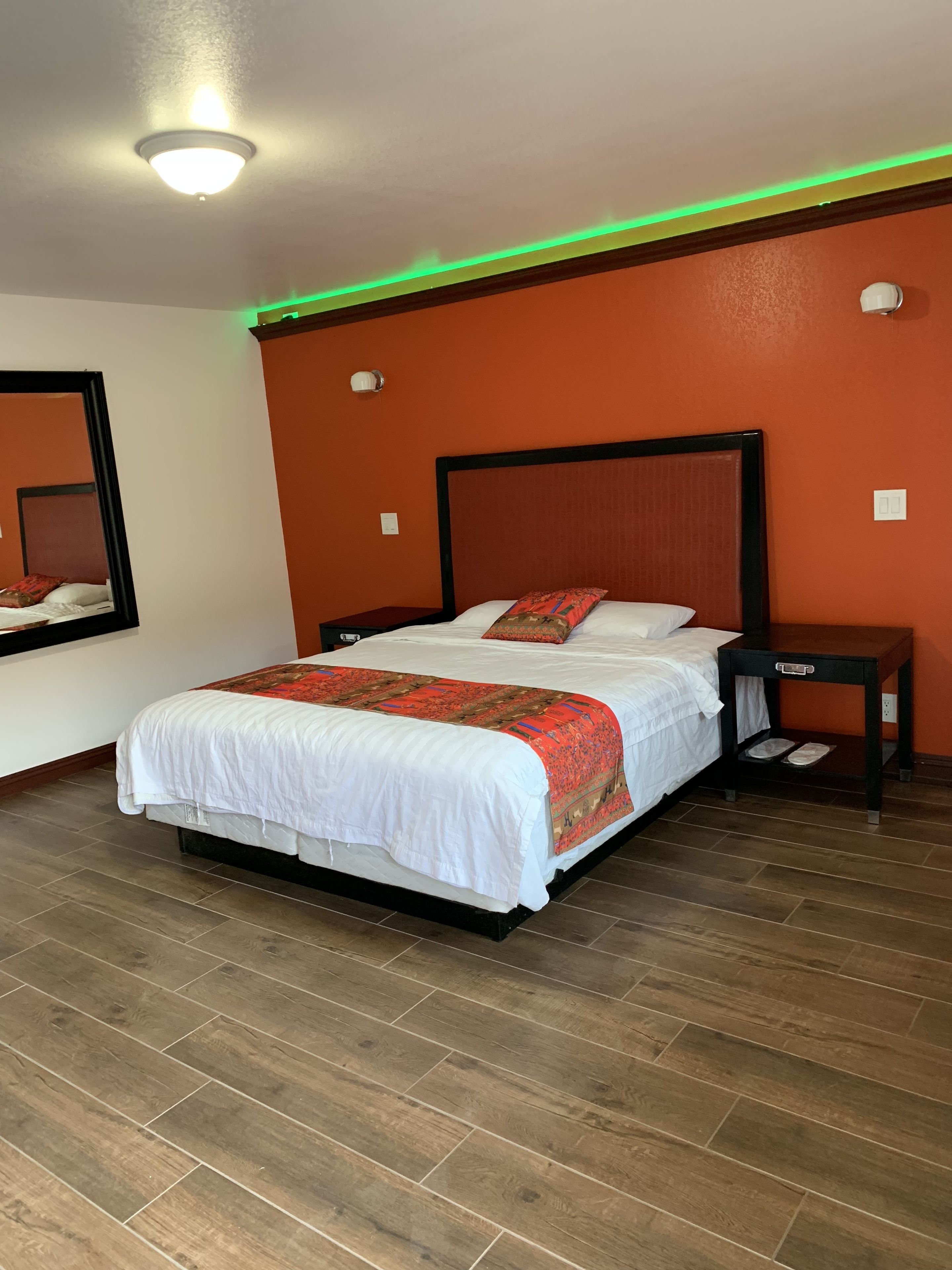 Una habitación de hotel con una cama grande, una mesita de noche, un espejo y una lámpara en el techo.