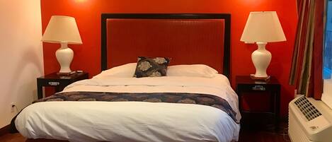 Quarto com piso de madeira, cama com roupa de cama branca, duas mesas de cabeceira com luminárias e um lustre.