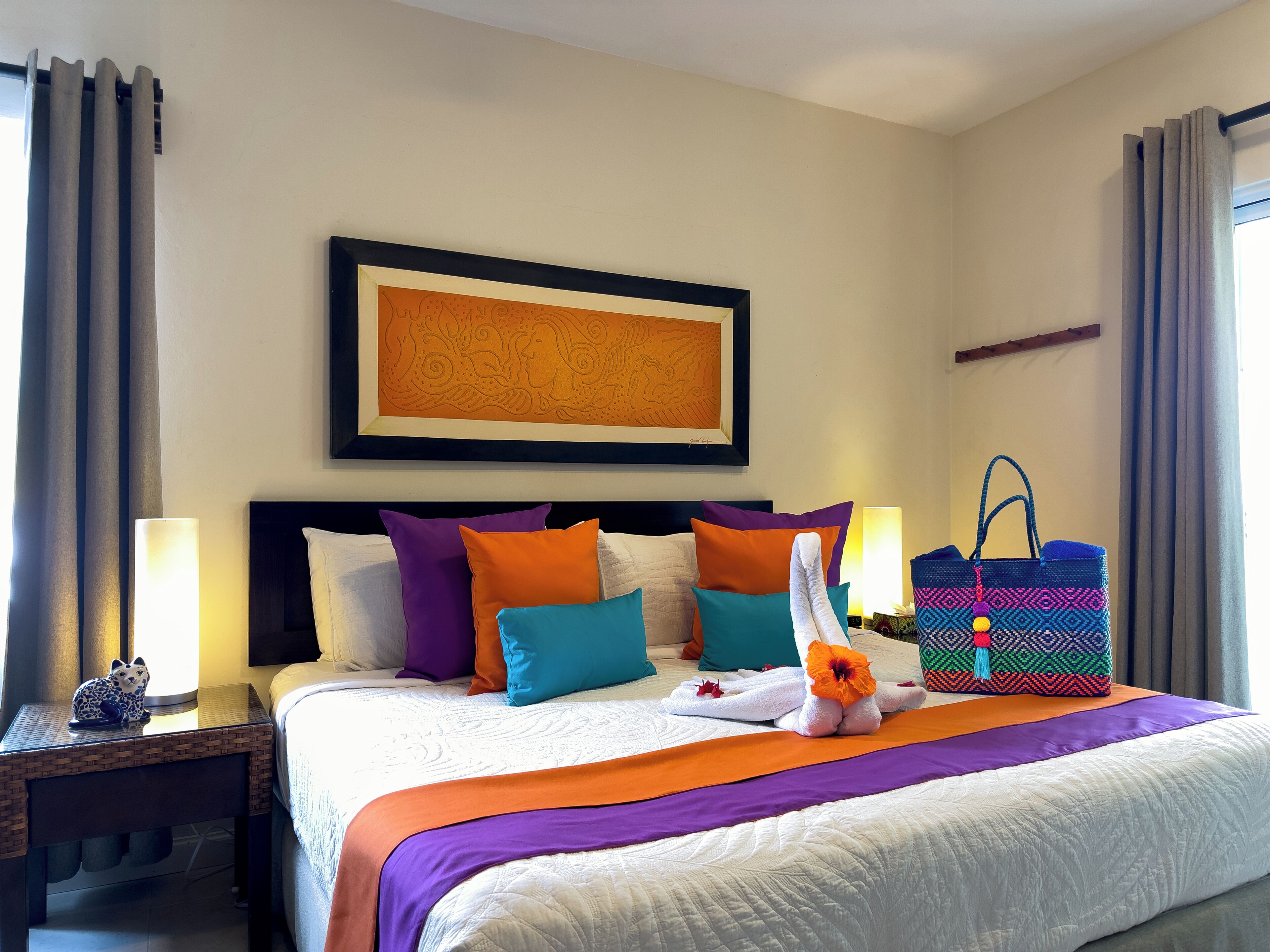 Habitació d'hotel amb llit, almoinades, una obra d'art emmarcada, una tauleta de nit, una làmpada, una bossa i cortines.
