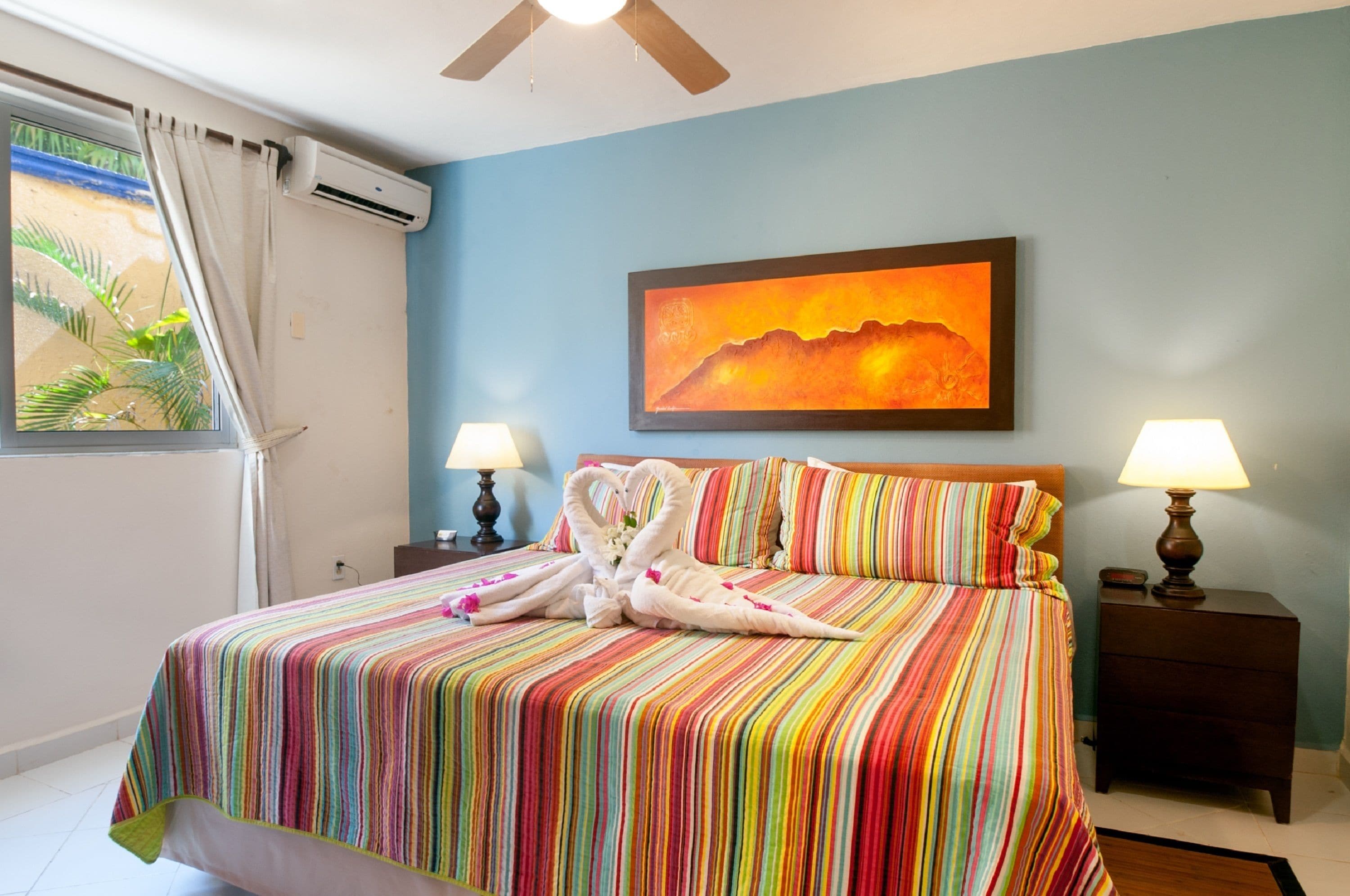 Quarto de hotel com cama, duas luminárias de cabeceira, um quadro na parede e um aparelho de ar condicionado.