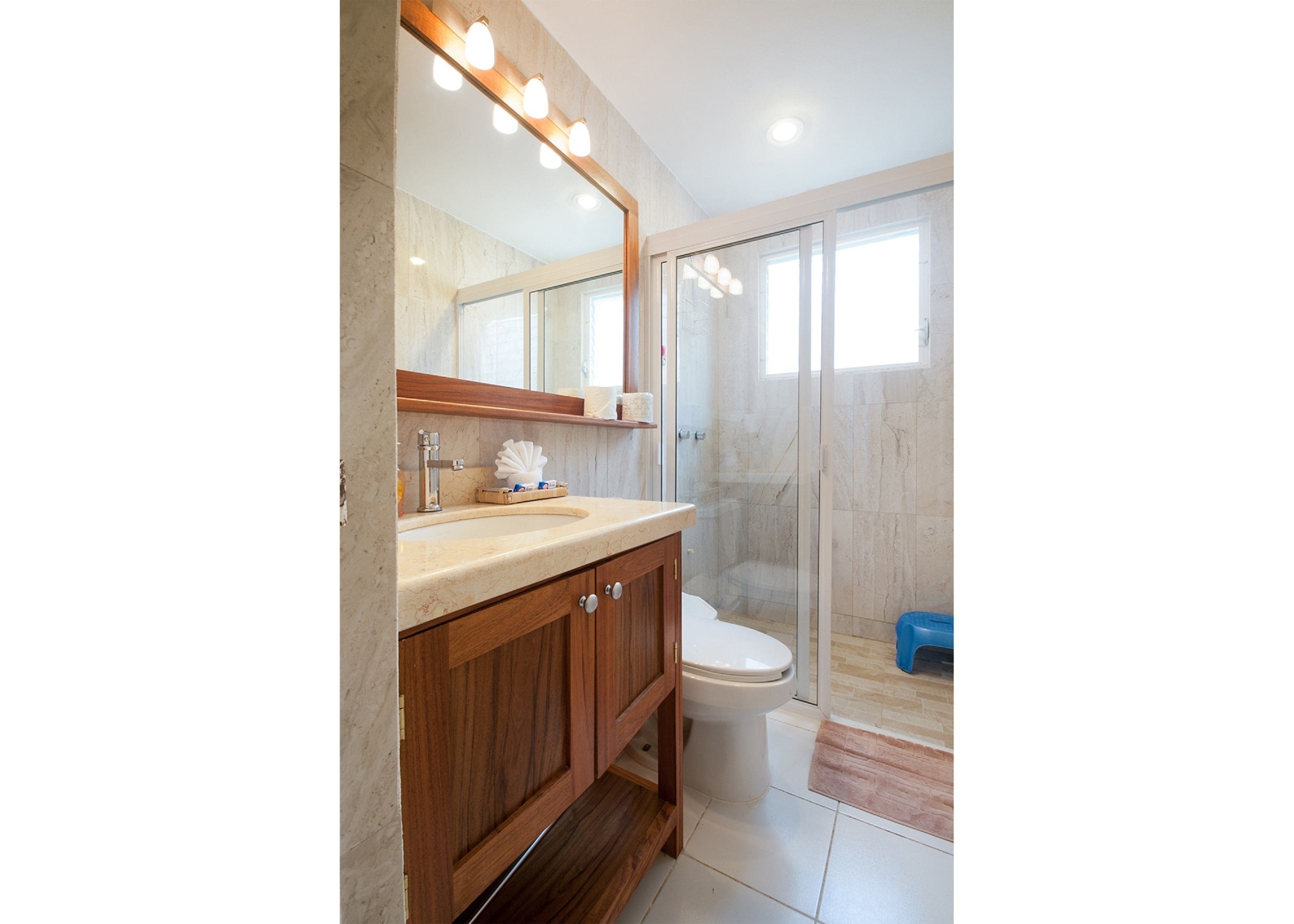A bathroom with a marble sink, wooden cabinets, a glass shower enclosure, and a toilet.