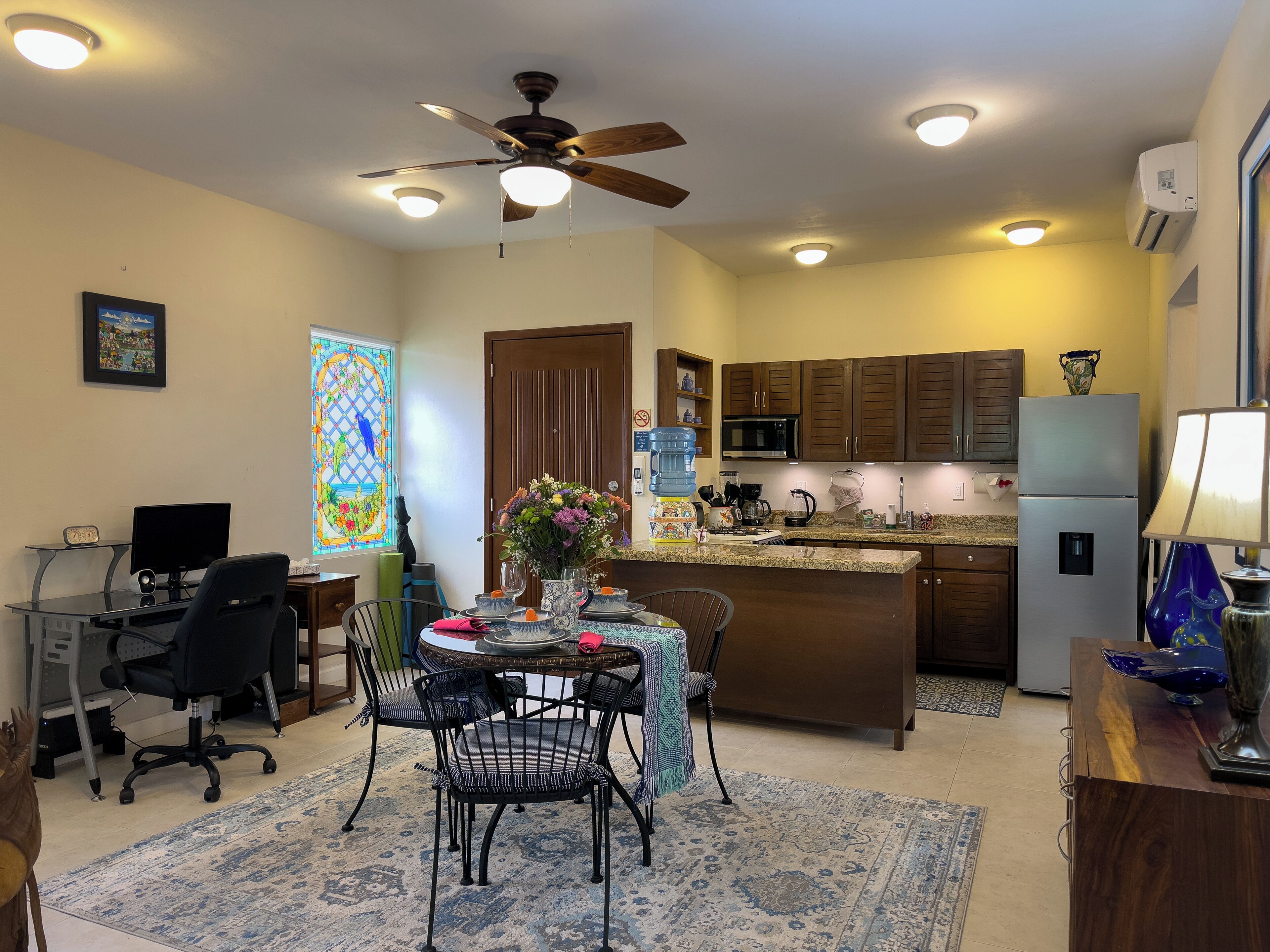 A modern kitchen with a dining area, a ceiling fan, a refrigerator, and a coffee maker.