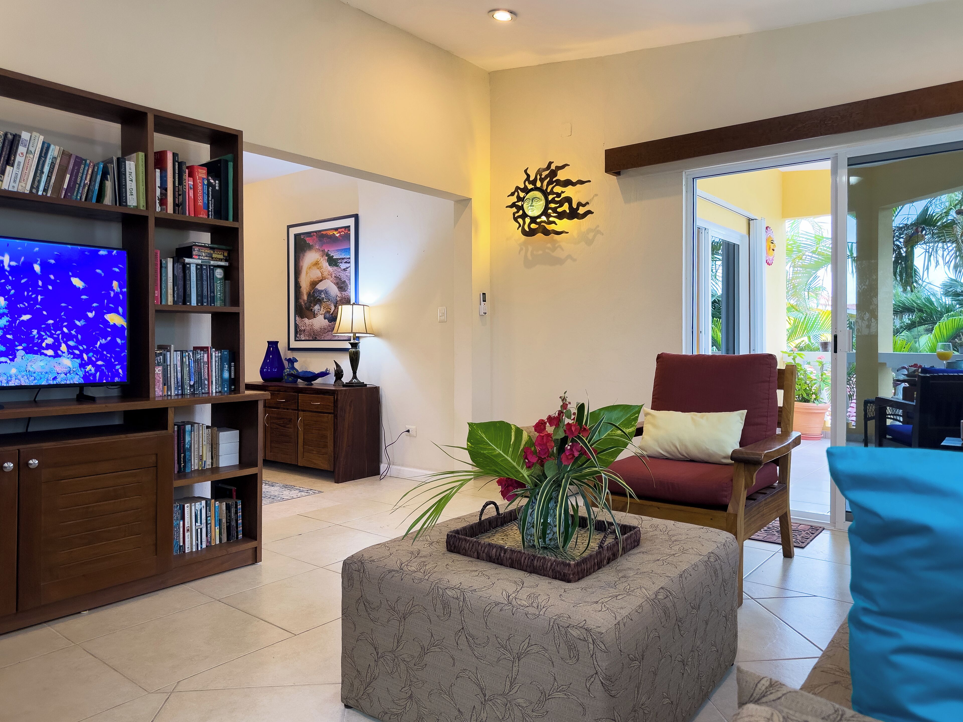 A living room with a television, bookshelf, decorative lamp, and a red chair.