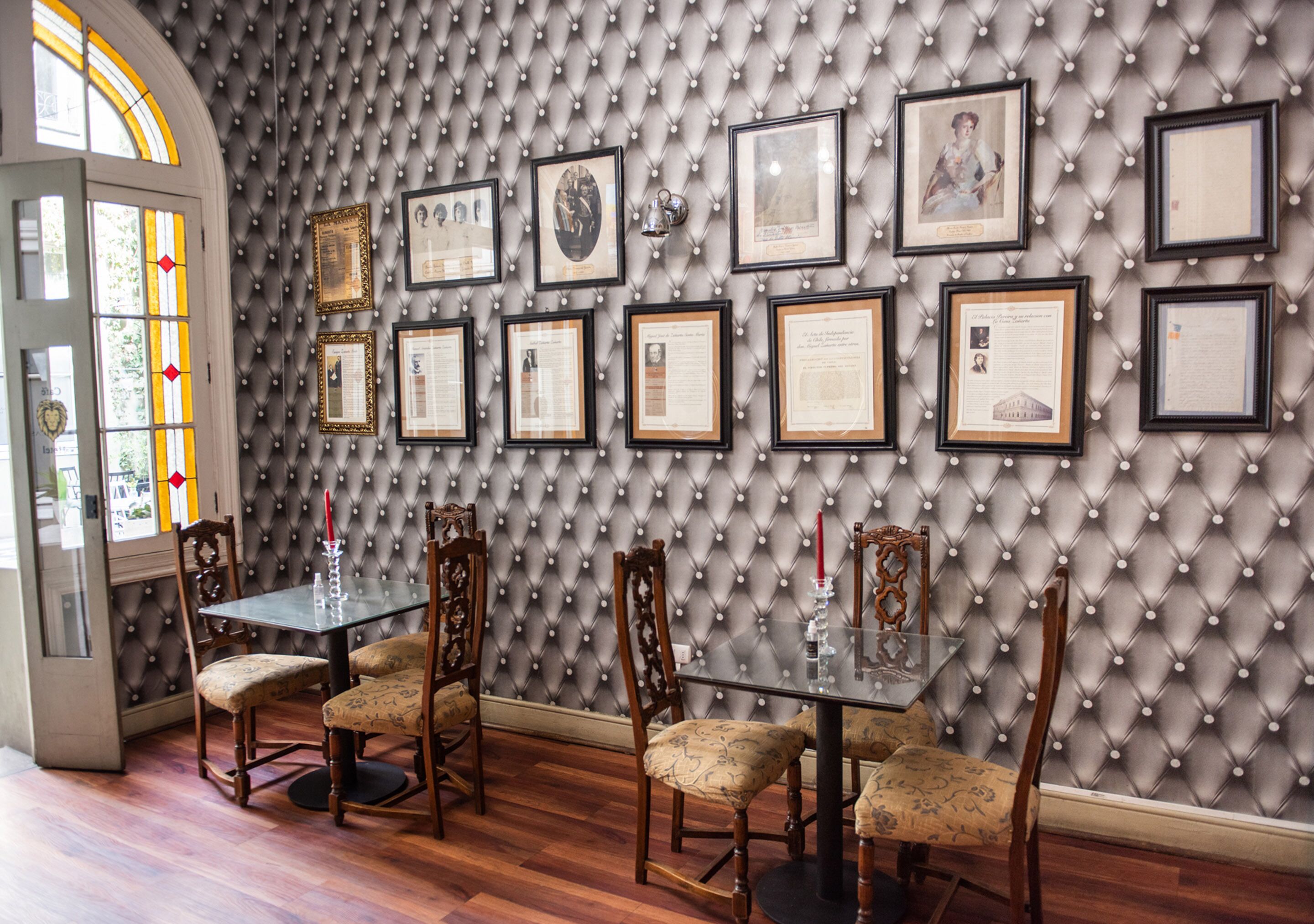 A dining area with a tufted wall, framed certificates, and a glass table with chairs.