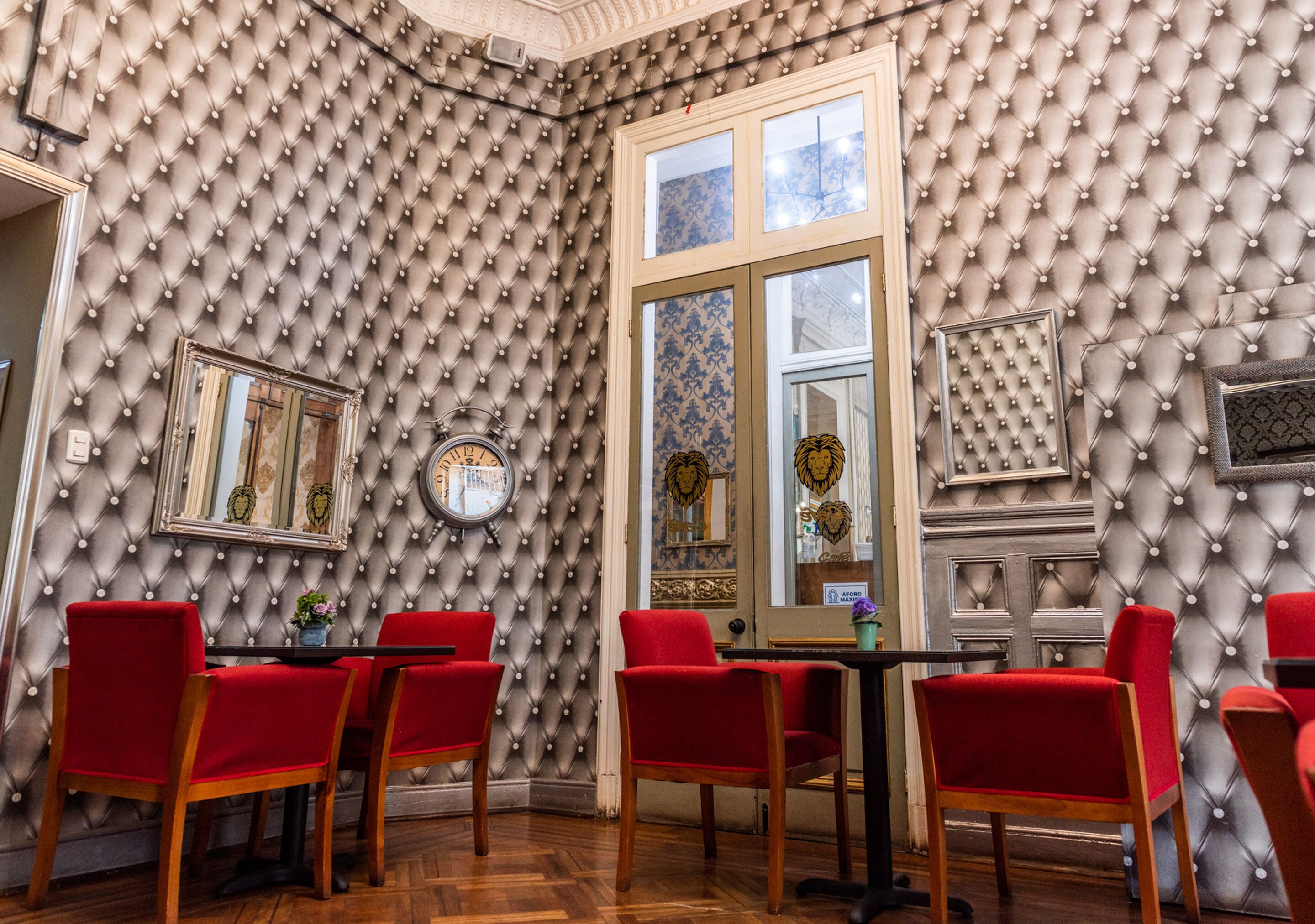 Una habitación con un cabecero capitonado, un reloj y sillones tapizados en rojo.