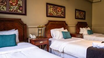 Ein Hotelzimmer mit drei Betten, Holz-Kopfteilen, weißen Laken und floralen Bildern an den Wänden.