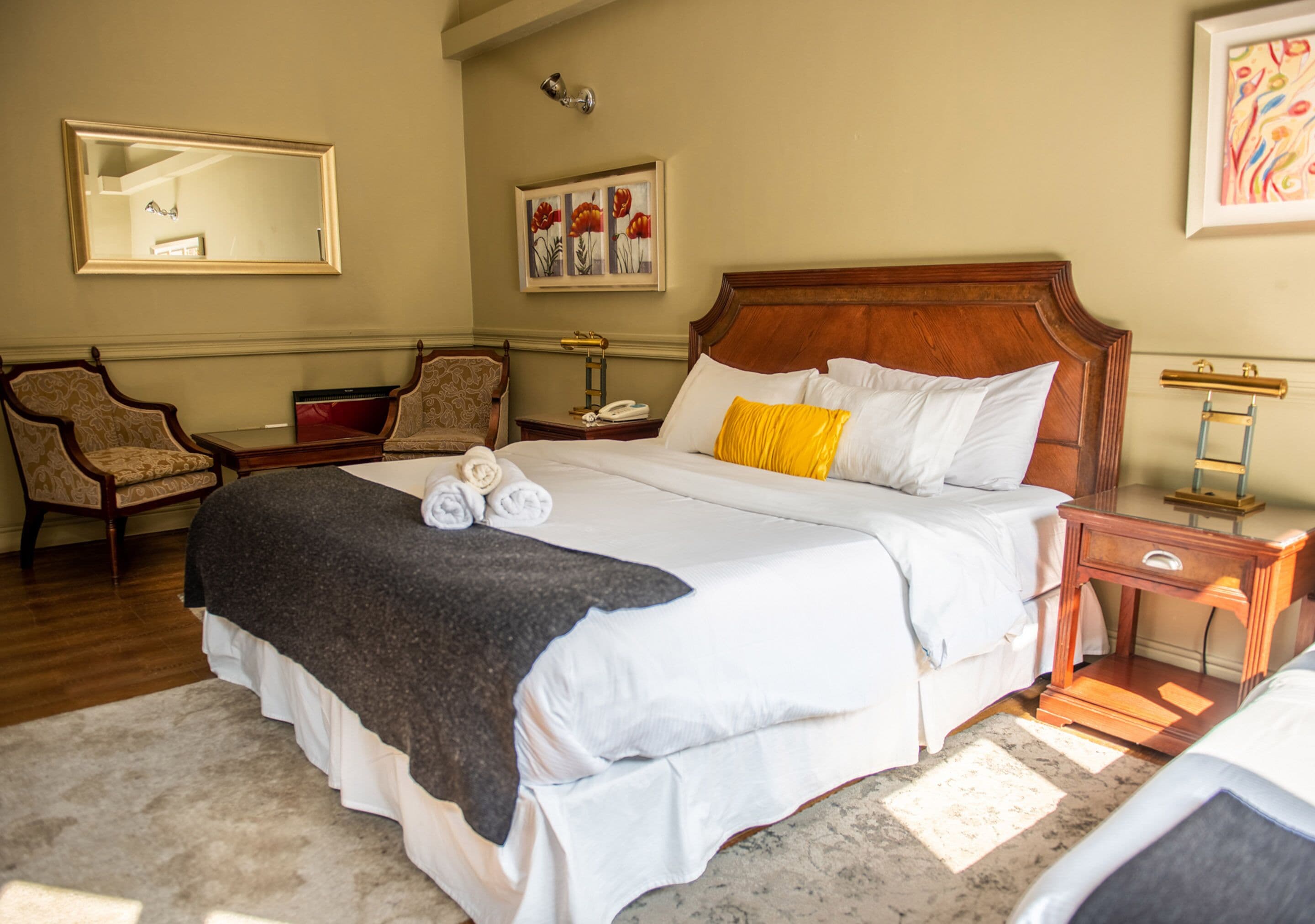 Une chambre d’hôtel avec un grand lit, une tête de lit en bois, une table de chevet avec une lampe, une chaise et un tableau au mur.