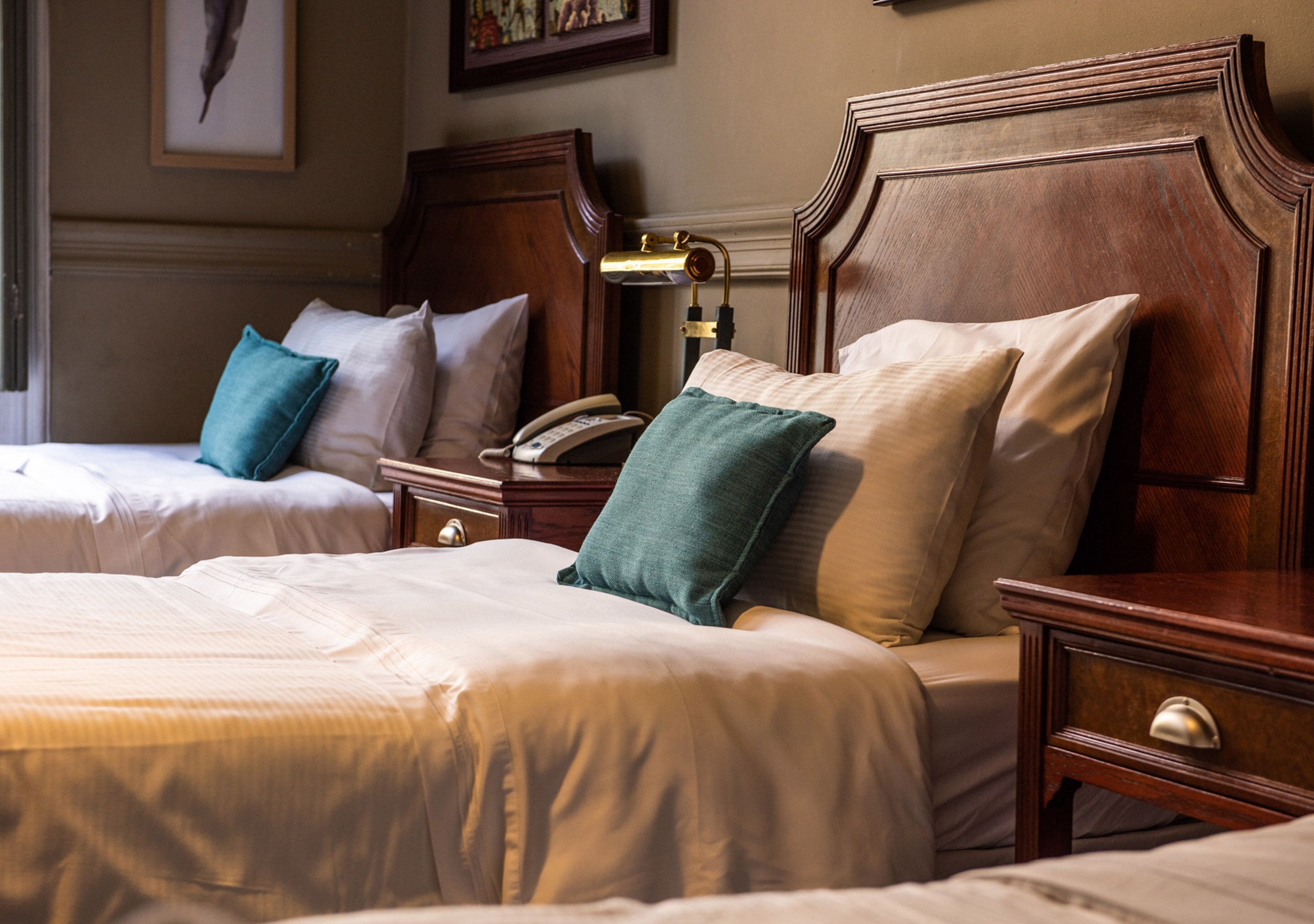 A hotel room with two beds, each with a wooden headboard, a bedside table with a lamp, and a telephone.
