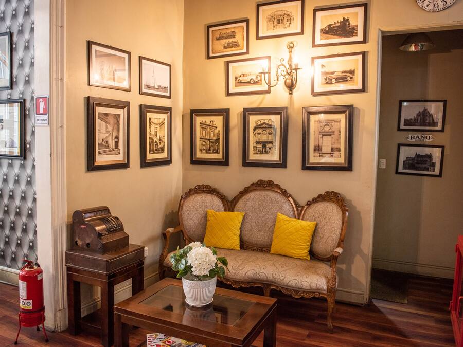 Una habitación con un sofá, una mesa de centro con un jarrón, cuadros en la pared y un extintor.
