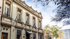 Un edificio histórico con detalles arquitectónicos ornamentados, varias banderas y una entrada porticada.