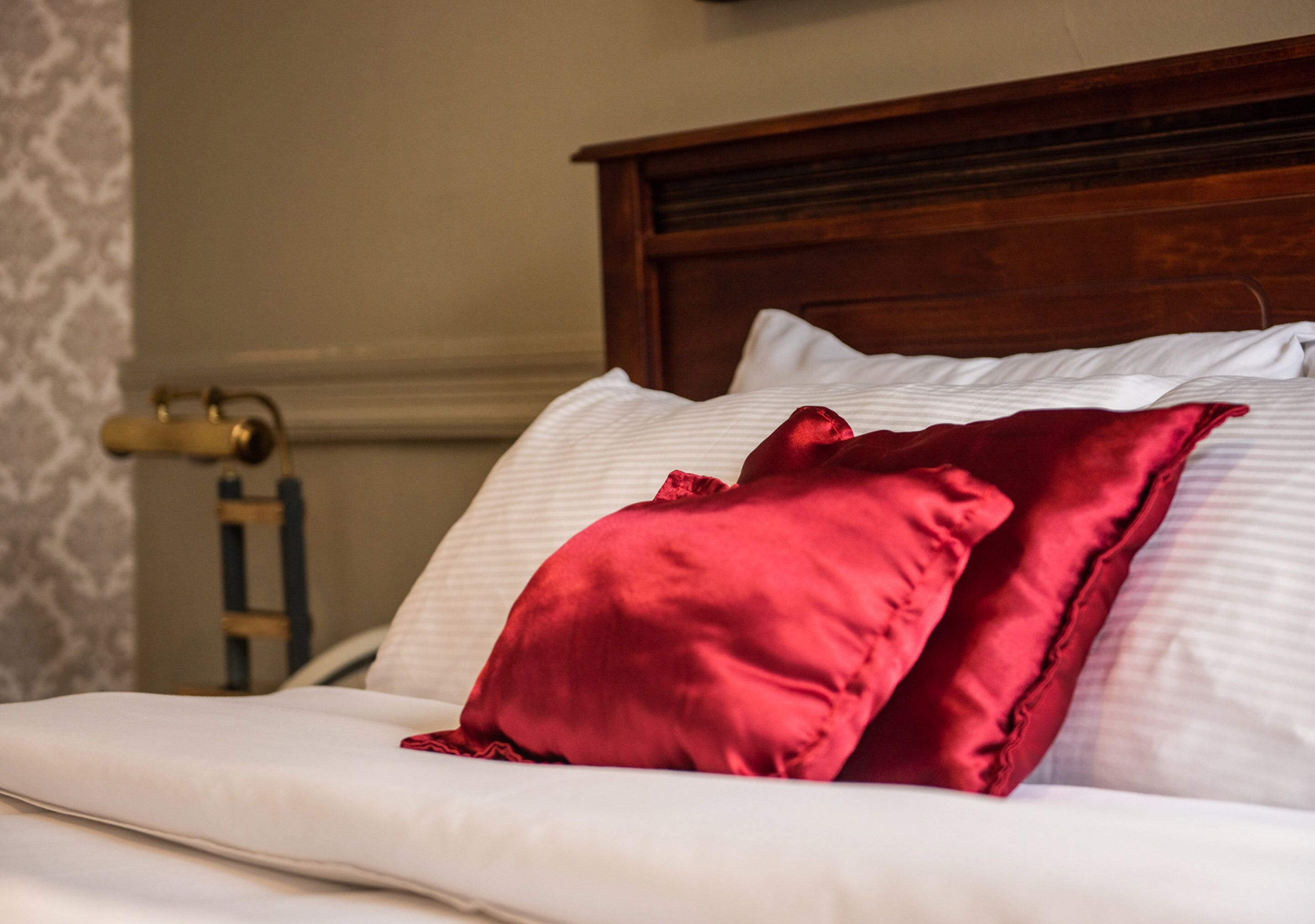 Una cama bien hecha con sábanas blancas y dos almohadas rojas.